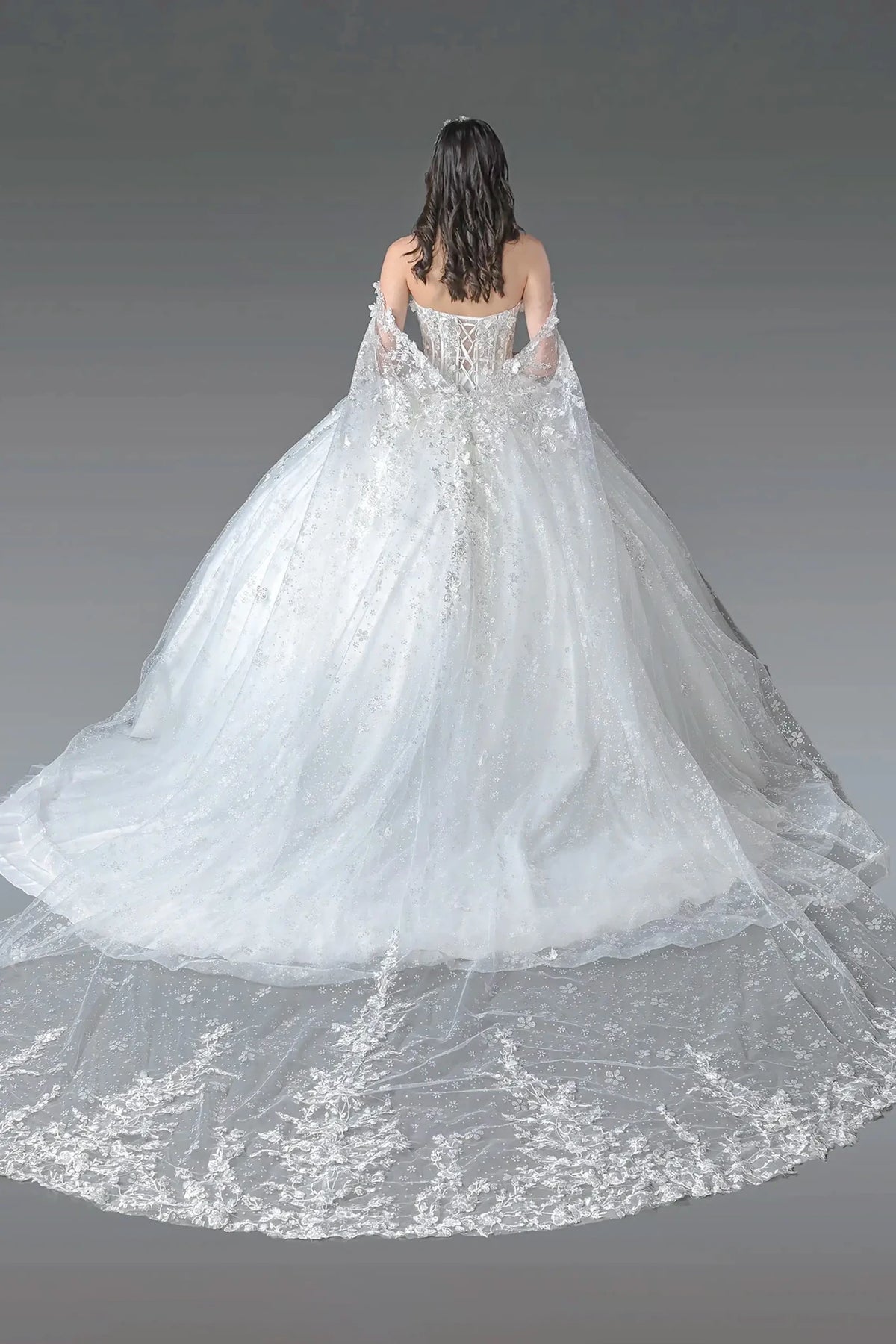 Woman wearing a white ball gown dress with intricate detailing and long trains on a gray background