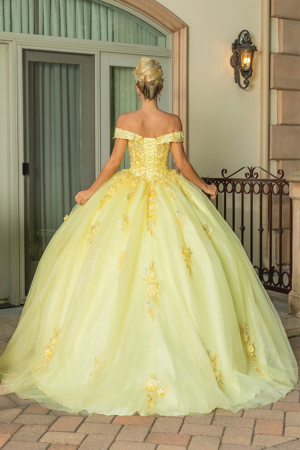 Revealing a lace-up bodice above its full tulle skirt, this Yellow quinceañera ball gown is shown from the back.