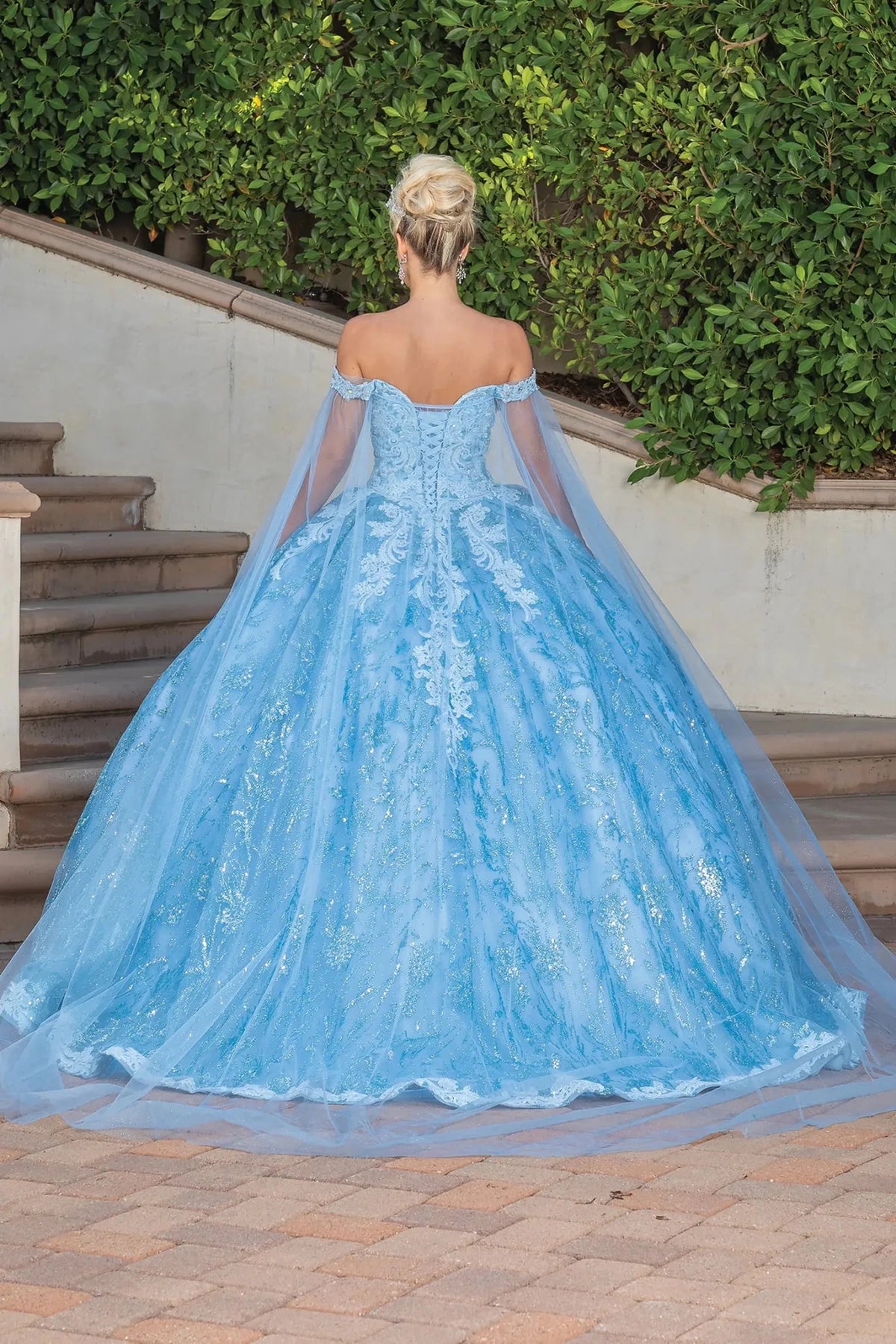 Back view of a Bahama Blue quinceañera gown showing lace-up back, sheer sleeves, and flowing train