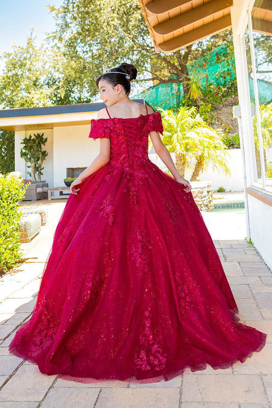 Young girl standing back-facing in Adriana mini quinceañera dress with lace-up bodice, glitter lace fabric, 3D floral sequin appliqués, and long flowing train