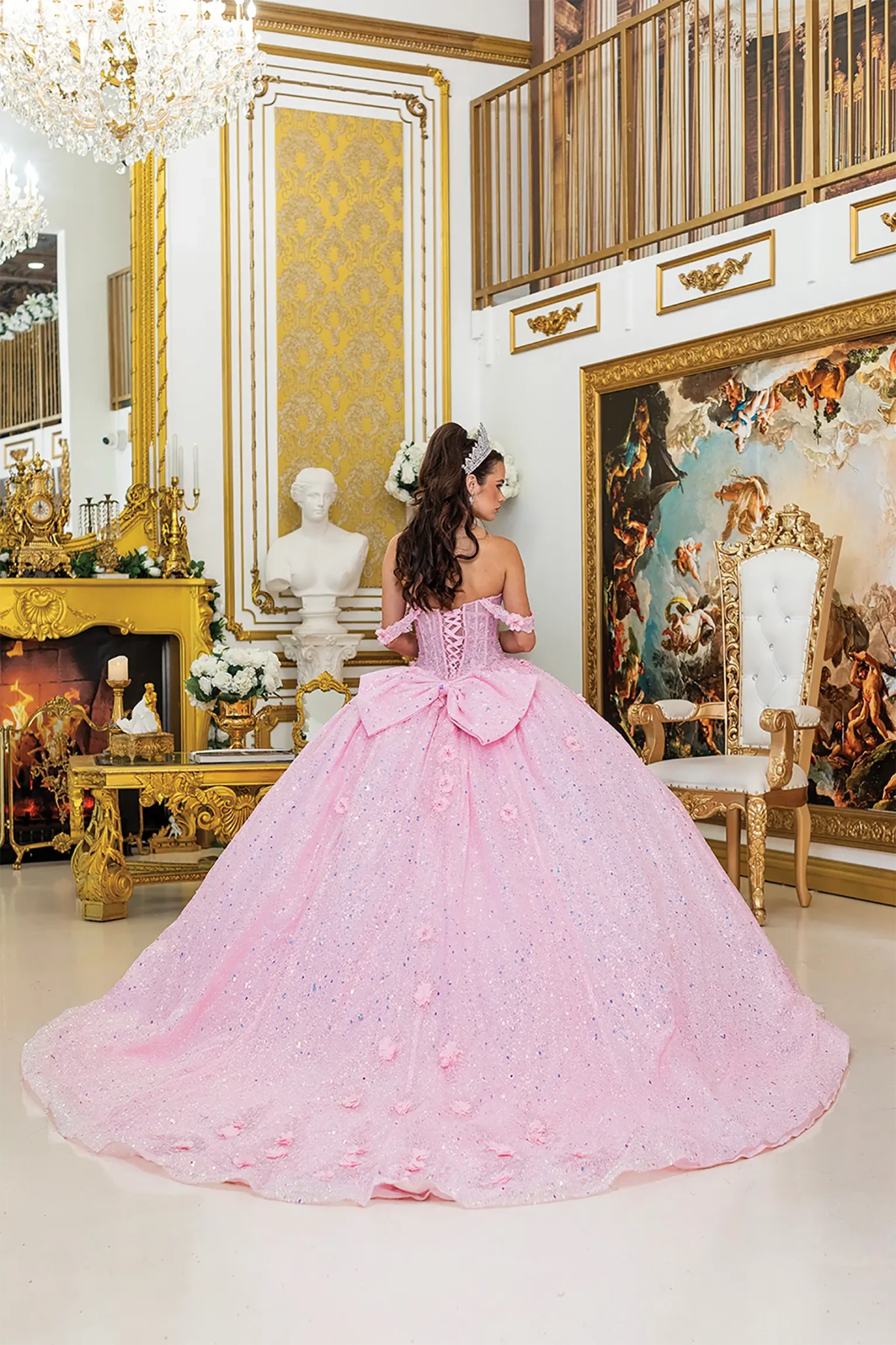 Back view of a woman wearing pink quinceañera dress featuring off-shoulder straps and layered glitter tulle skirt