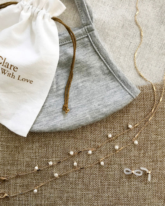 Pearl and gold chain eye wear necklace on a textured surface with a pouch.