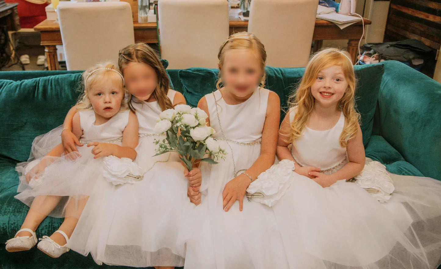 Four young girls in white dresses sitting on a green couch.