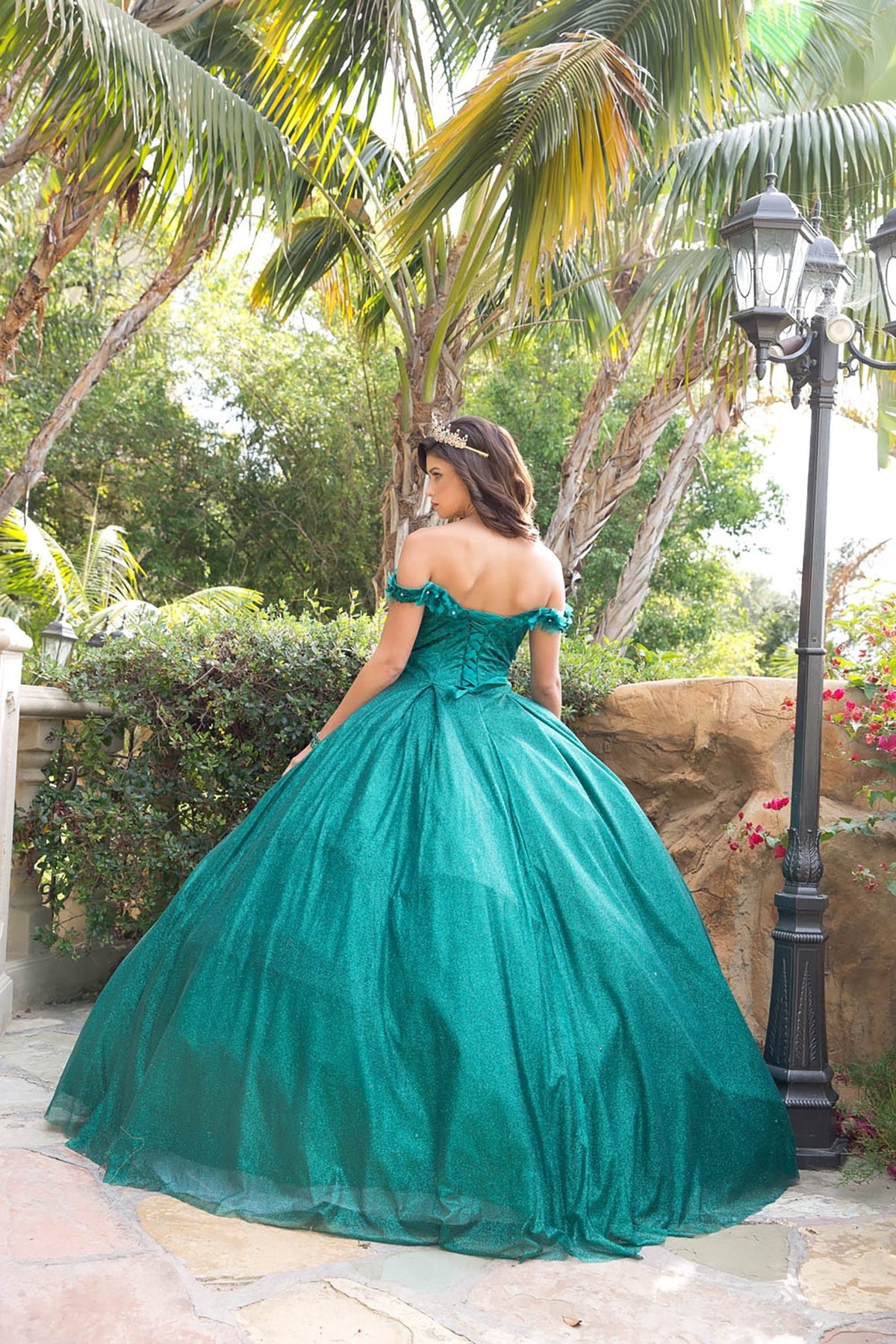 Back view of a woman wearing a hunter green quinceañera dress with lace-up corset back, floral applique and tulle skirt