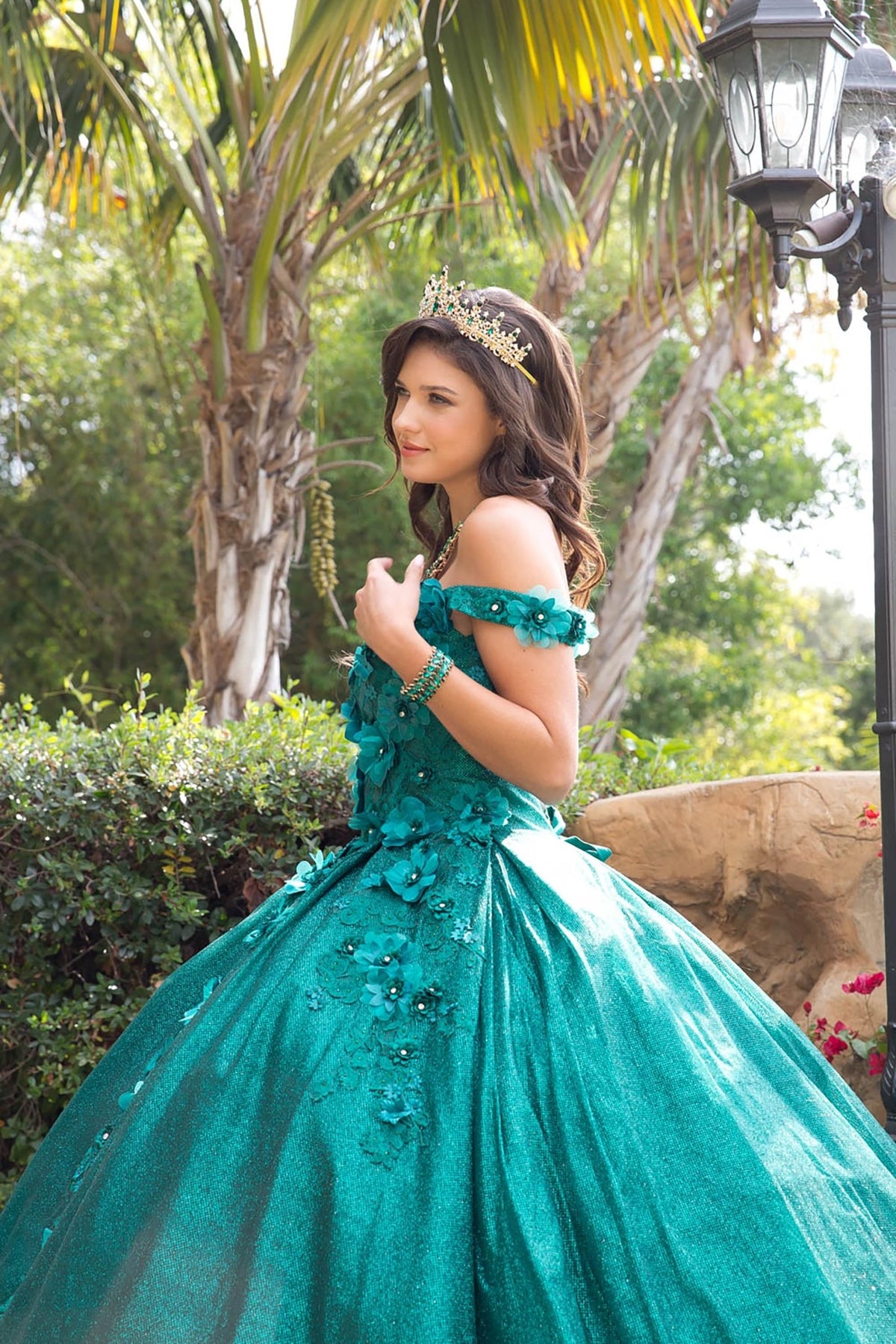 Side view of a woman wearing a hunter green quinceañera dress with off-shoulder sleeves, floral applique and tulle skirt