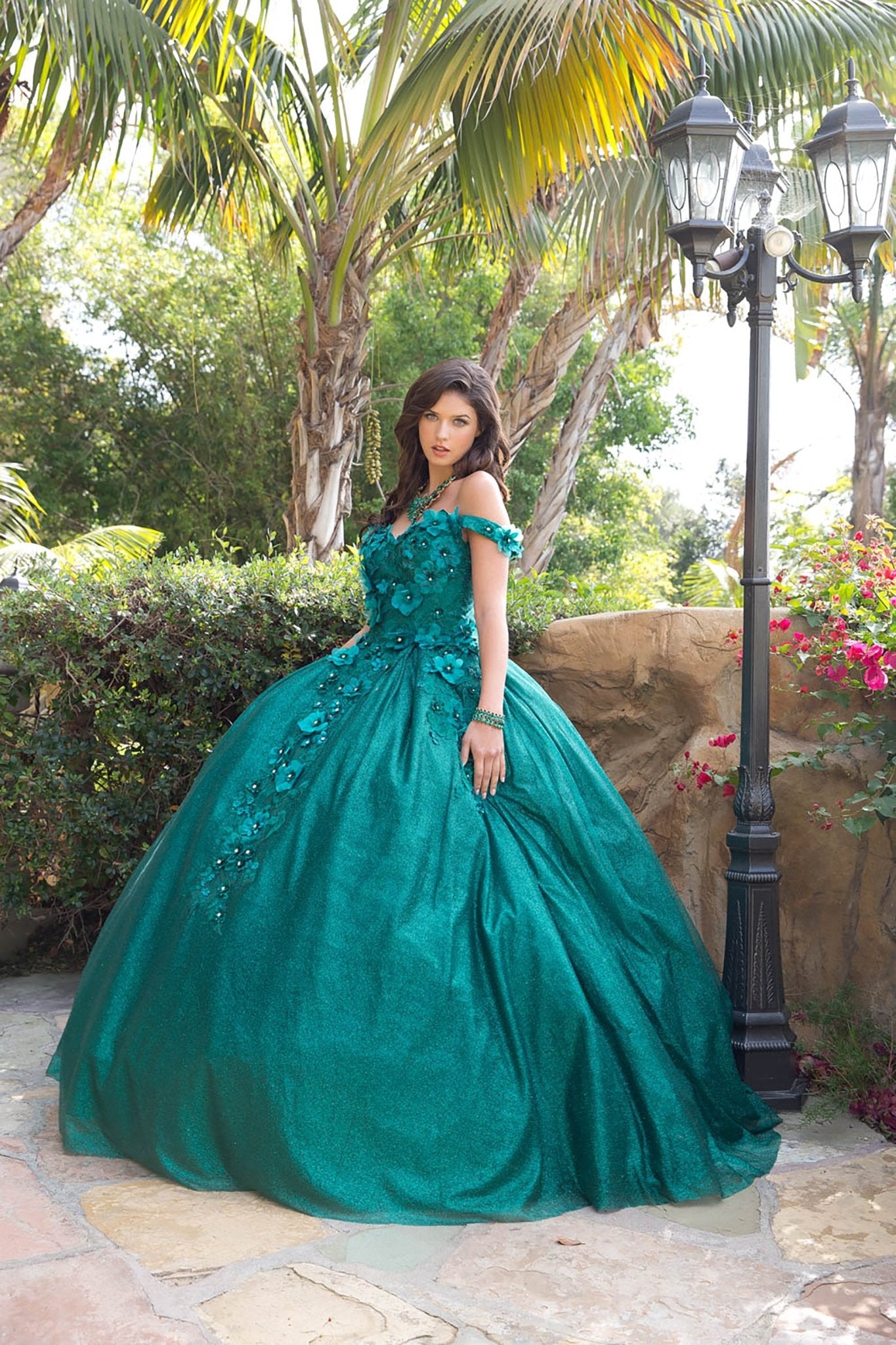 Three-quarter front view of a woman wearing a hunter green quinceañera dress with floral applique, corset bodice and tulle