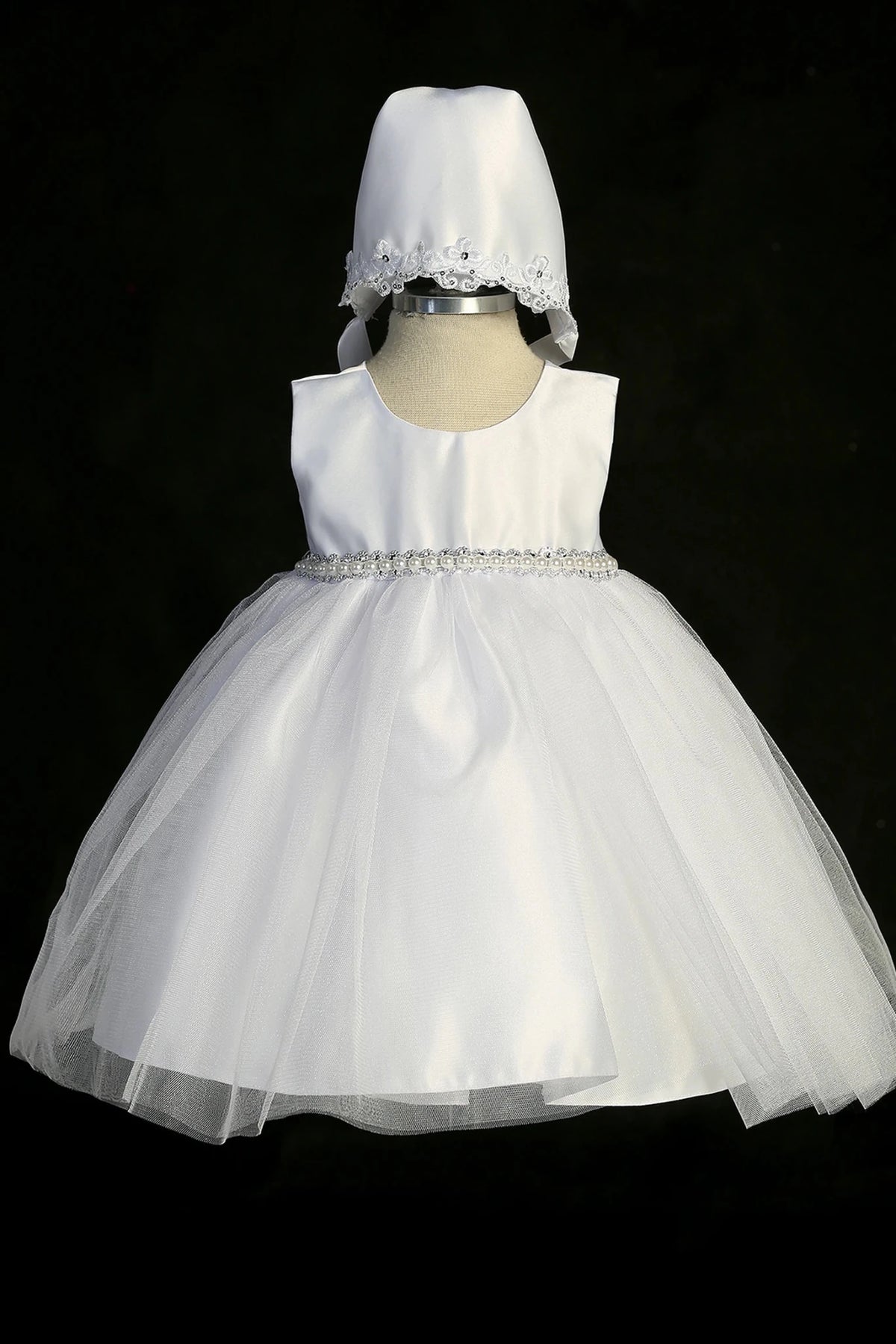 Detail of the white christening dress showing tulle overlay skirt and large satin bow.