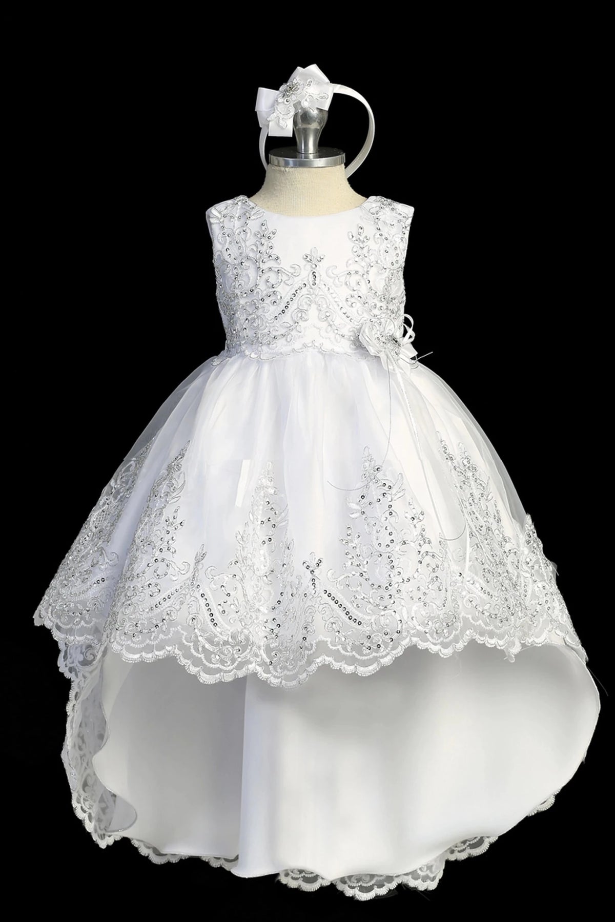 Detail of the white baptism dress showing high-low organza skirt with a lace-appliqué hem.