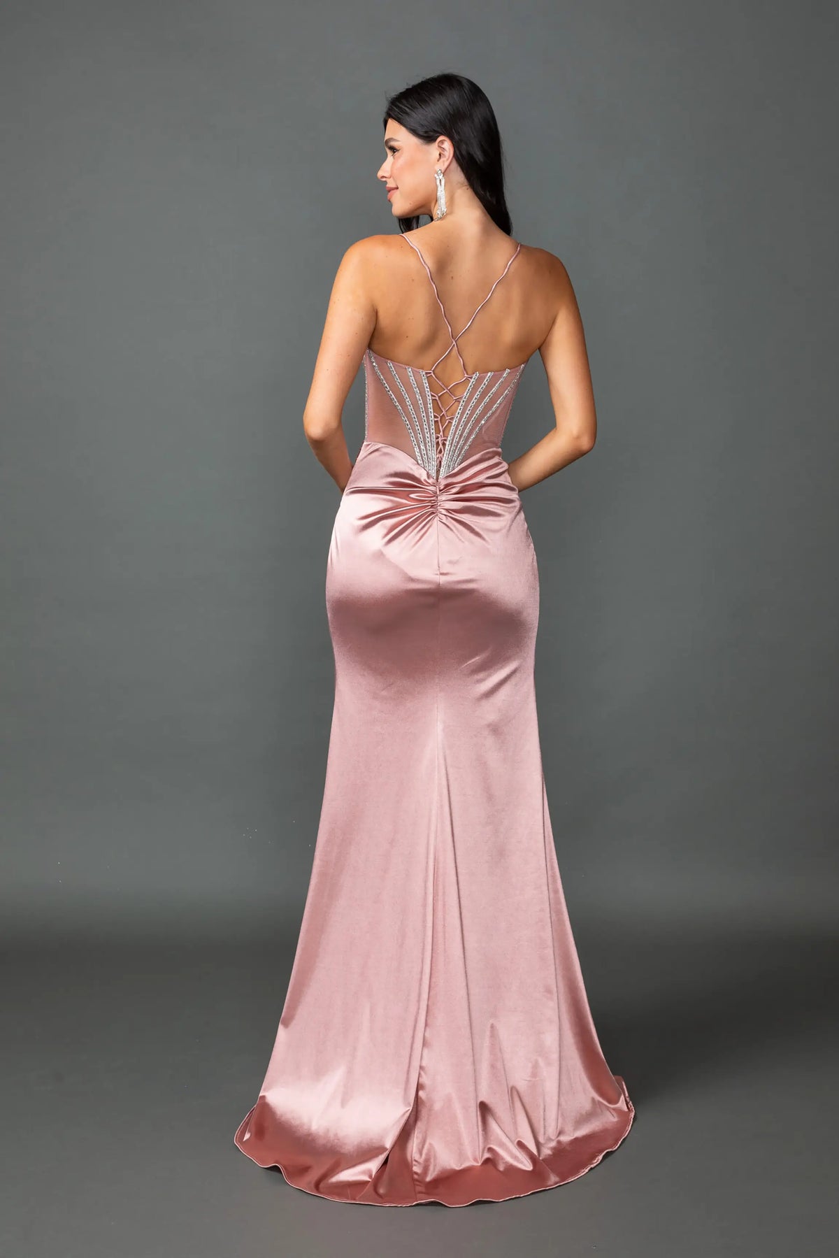 Revealing crisscross straps above its satin skirt, this Rose Gold prom dress is shown from the back.