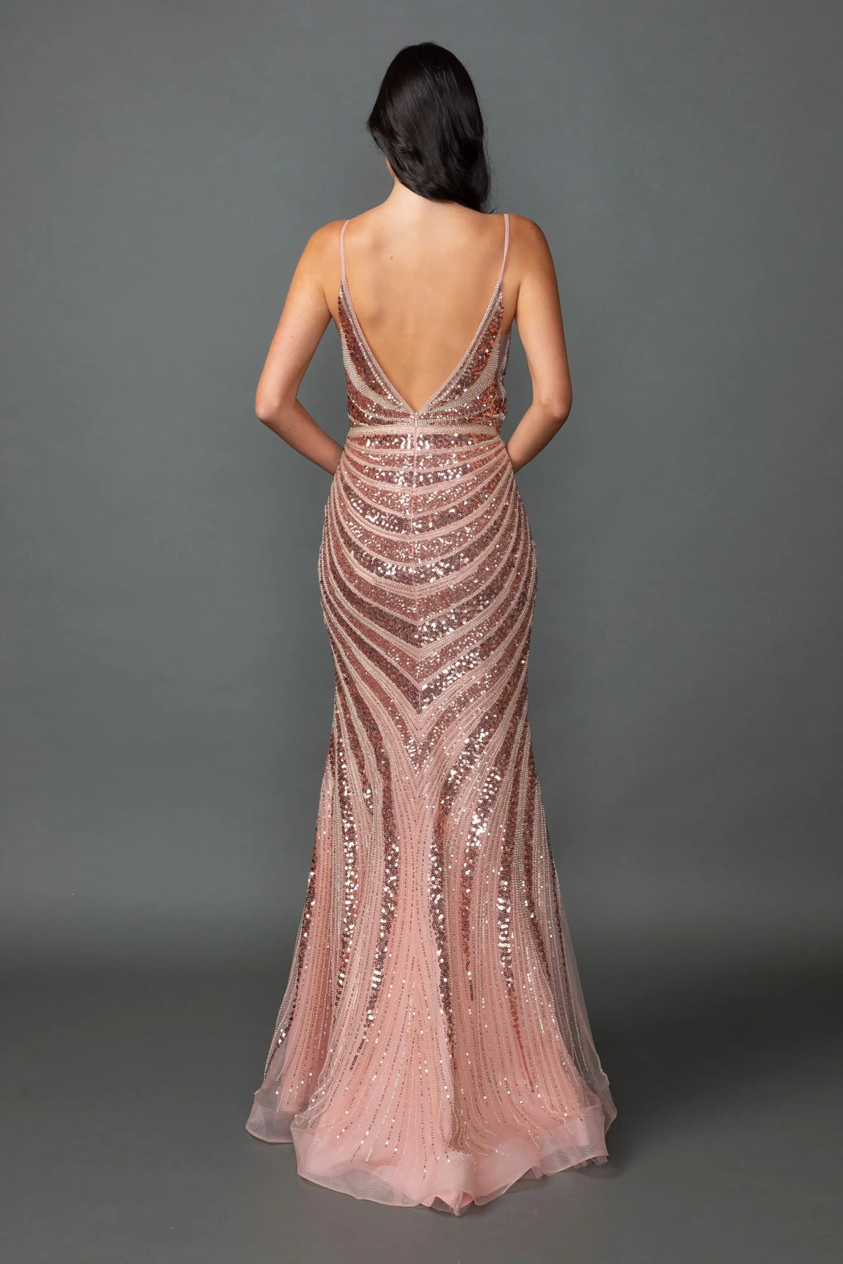 Revealing decorative sequin patterning around its open back, this Rose Gold prom dress is shown from the back.