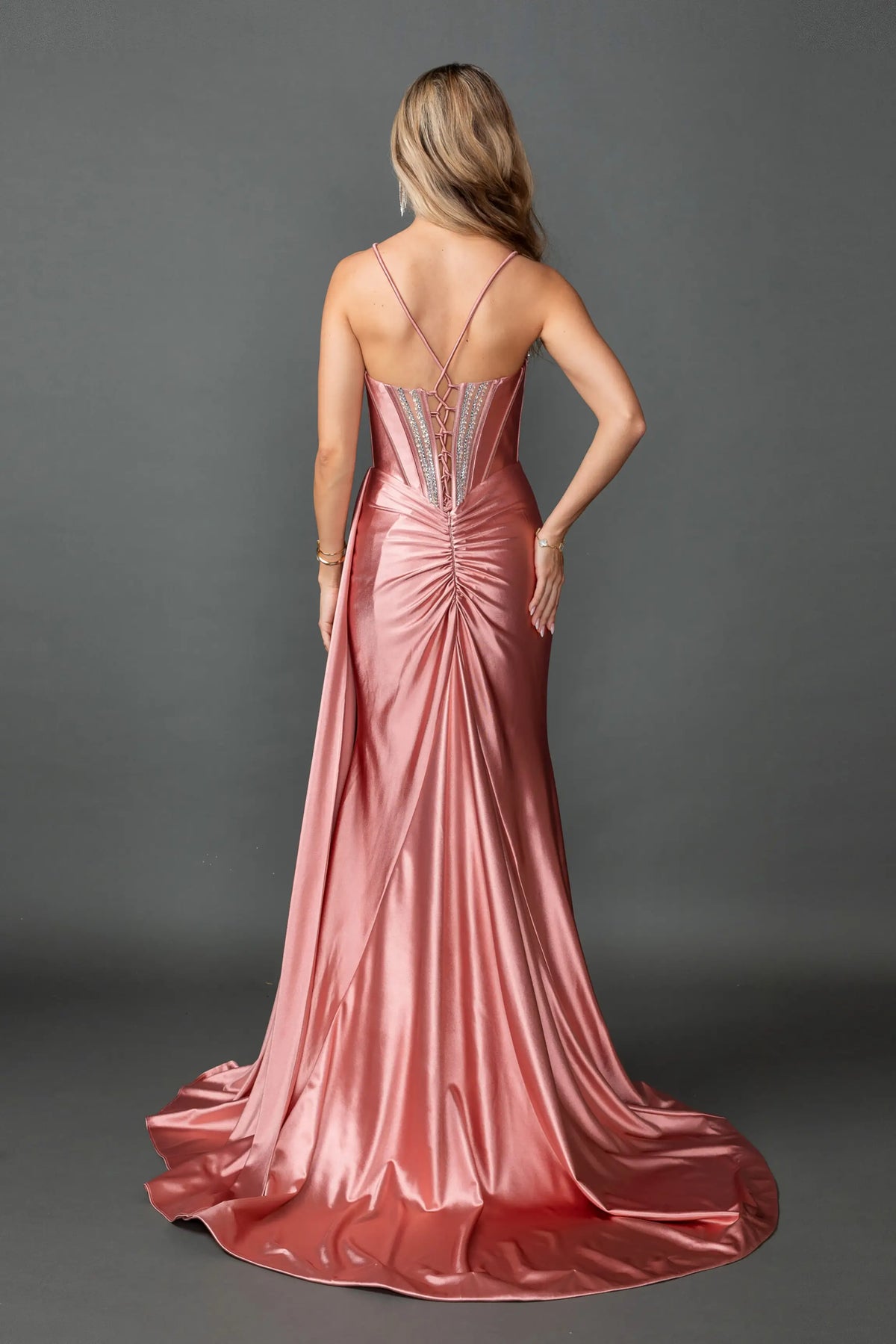 Revealing crisscross straps above its gathered satin train, this Rose Gold prom dress is shown from the back.