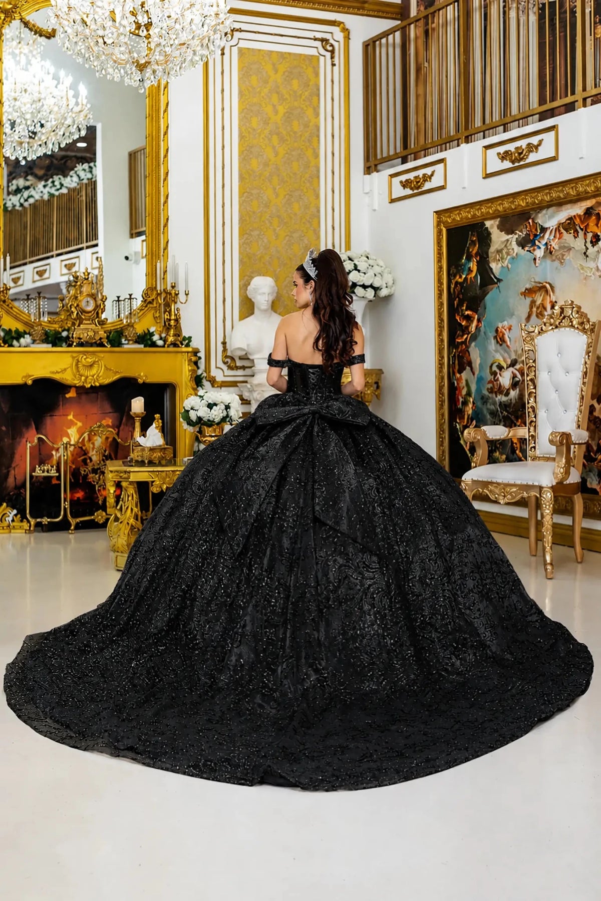 Black quinceanera ball gown back view showing lace up corset back, oversized layered bow detail, shimmering tulle skirt, and sweeping train