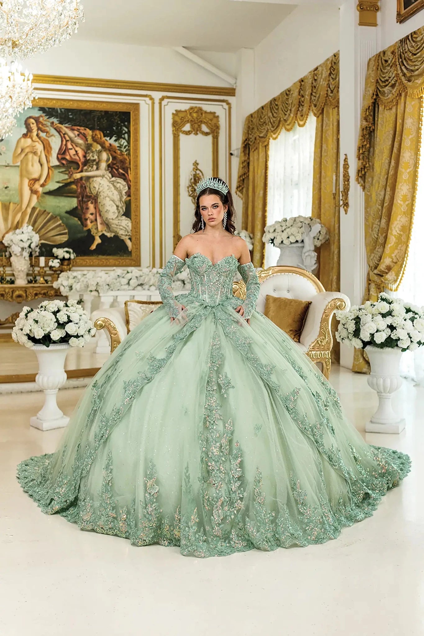 Woman standing front facing in lilac-sage quinceañera ball gown with off-shoulder floral appliqués, corset bodice, glittered tulle skirt, and delicate layered detailing