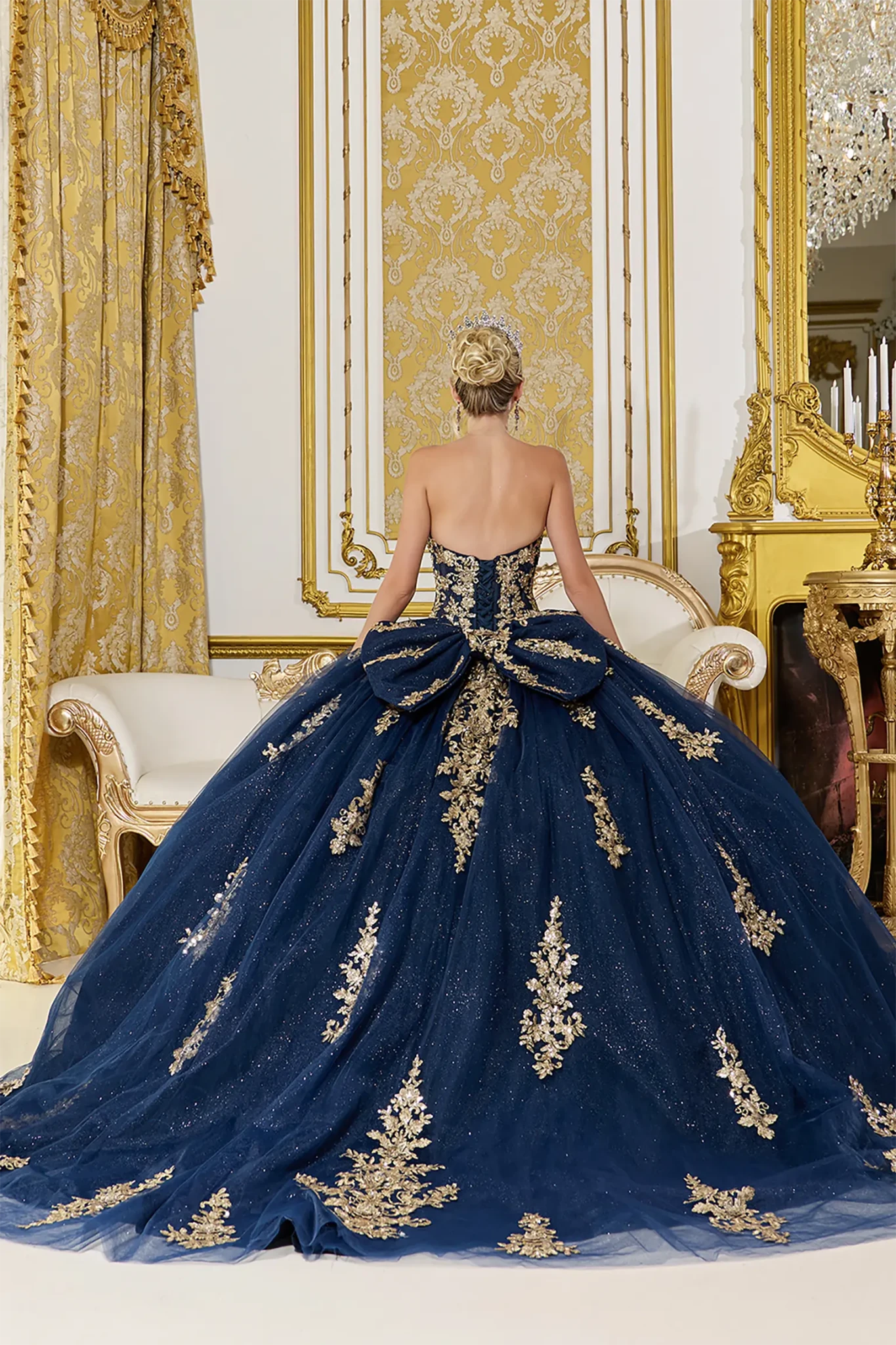 Back view of a woman wearing navy quinceañera dress featuring lace-up corset back and layered glitter tulle skirt