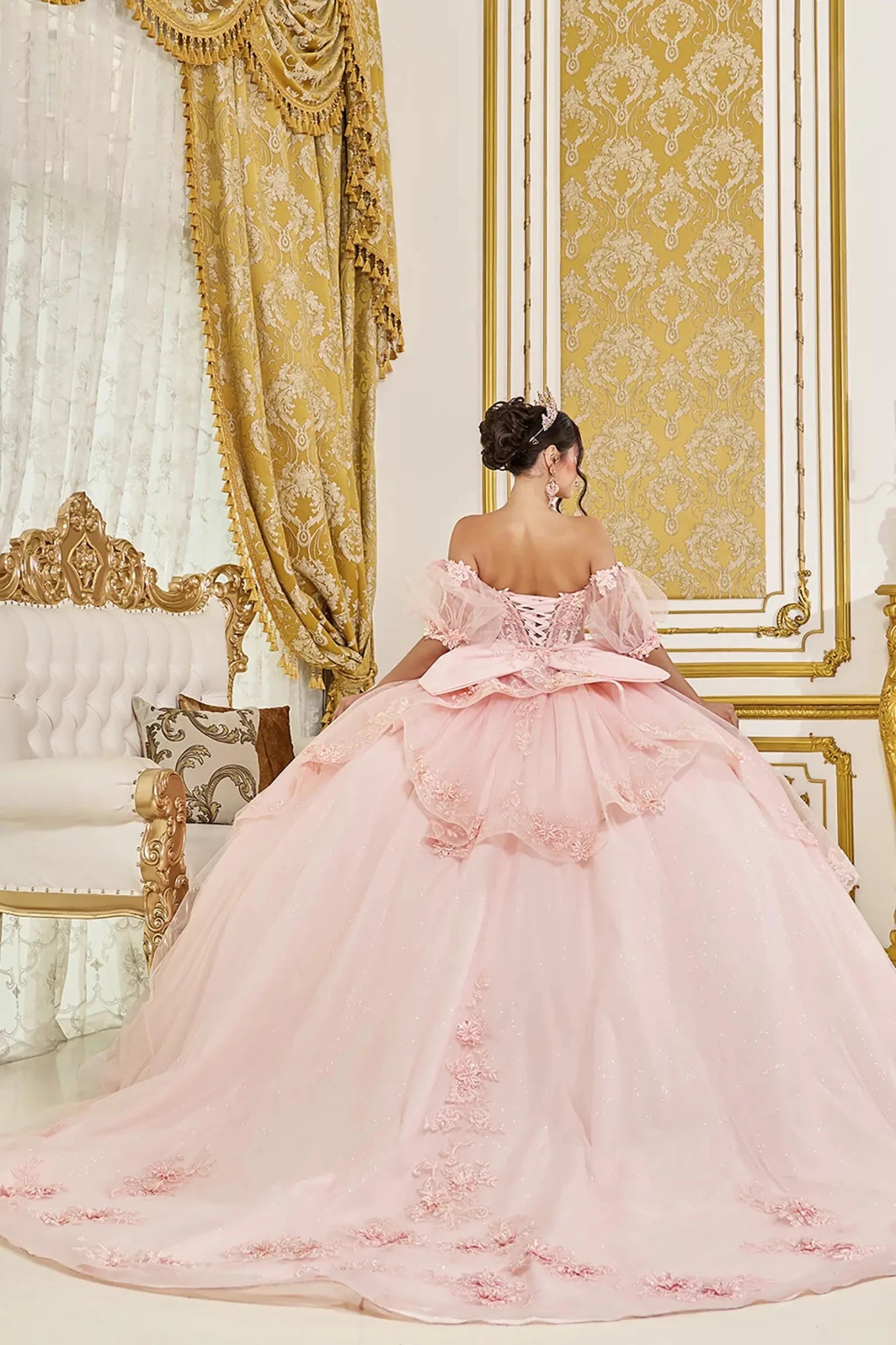 Blush quinceanera ball gown back view showing lace up corset, dramatic layered tulle overskirt, and structured bow detail