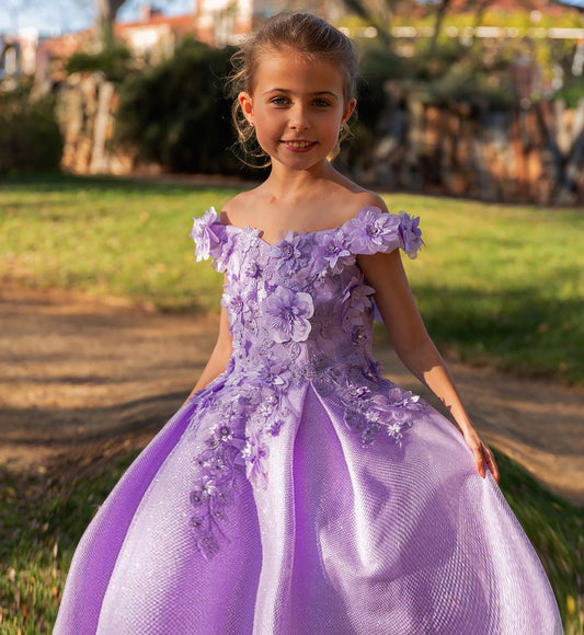Young girl in a purple floral dress standing outdoors with greenery in the background