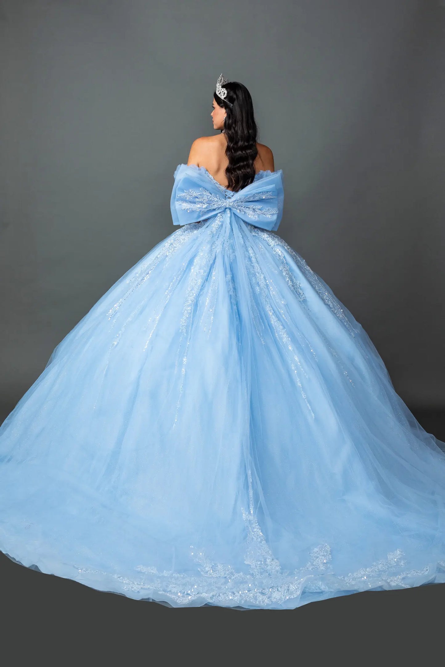 Back view of a woman in a bahama blue quinceañera ball gown featuring lace-up corset Back with big Back bow