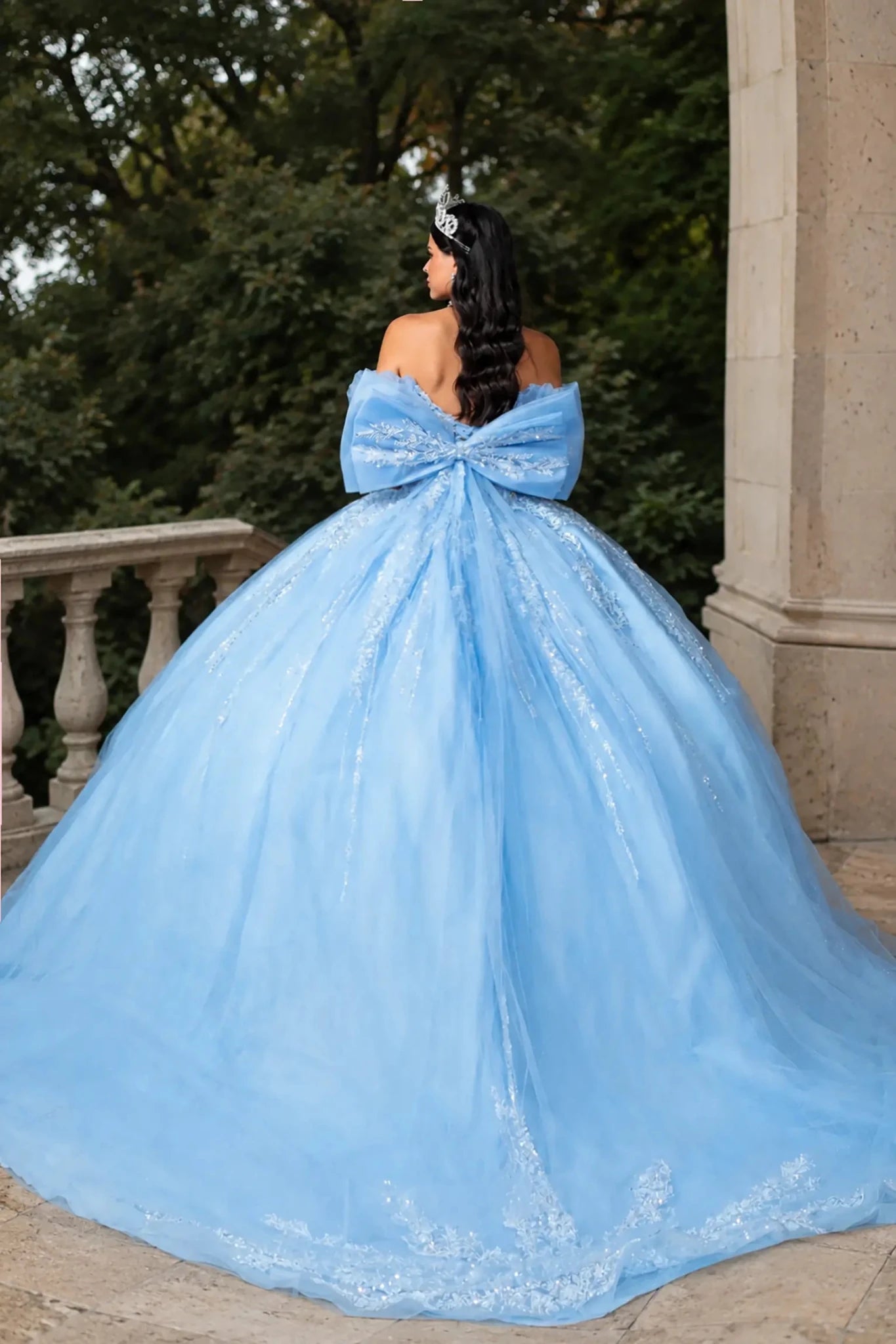 Back view of a woman in a bahama blue quinceañera ball gown featuring lace-up corset Back with big Back bow