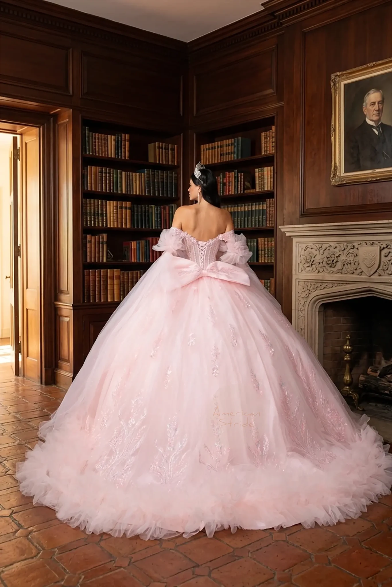 Back view of a girl wearing off‑shoulder sweetheart blush quinceañera ball gown featuring lace‑up corset closure, 3D floral appliqué, layered ruffle skirt, and detachable puff sleeves