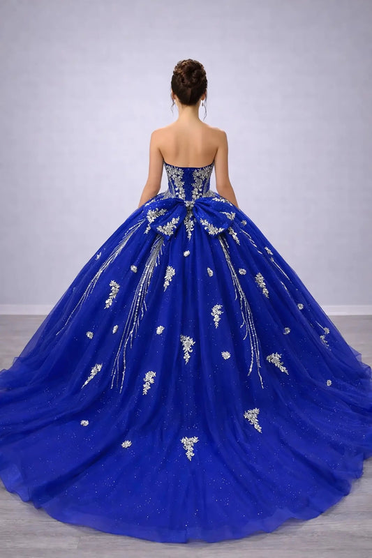 Woman standing back-facing in royal blue ball gown with lace-up corset bodice and cascading layered tulle skirt