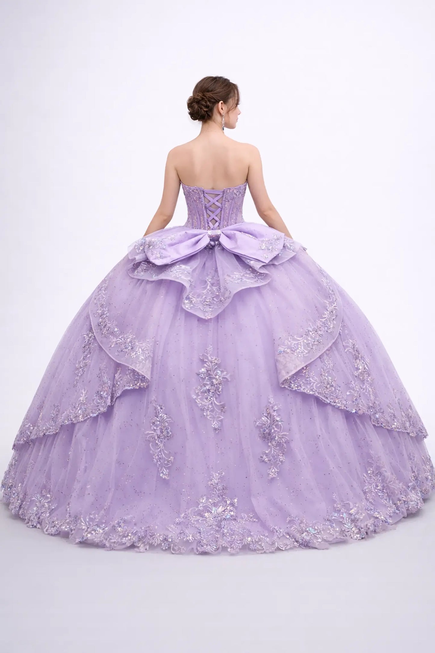 Back view of a woman wearing lilac quinceañera, lace-up corset, layered tulle overskirt and embroidered appliques
