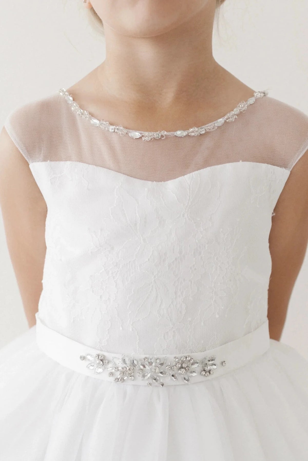 Crystal edging traces the off-white flower girl dress's sheer neckline.