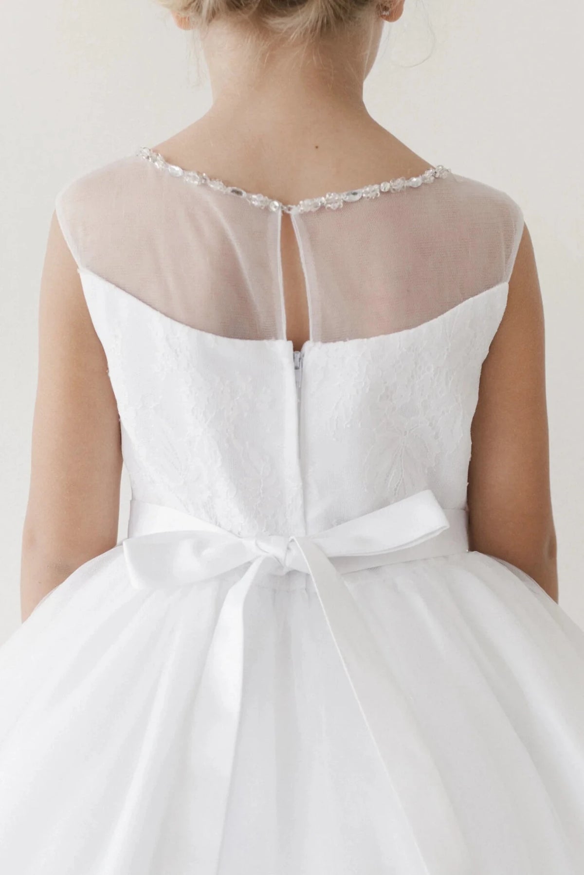 Sheer mesh spans the off-white flower girl dress's upper back.