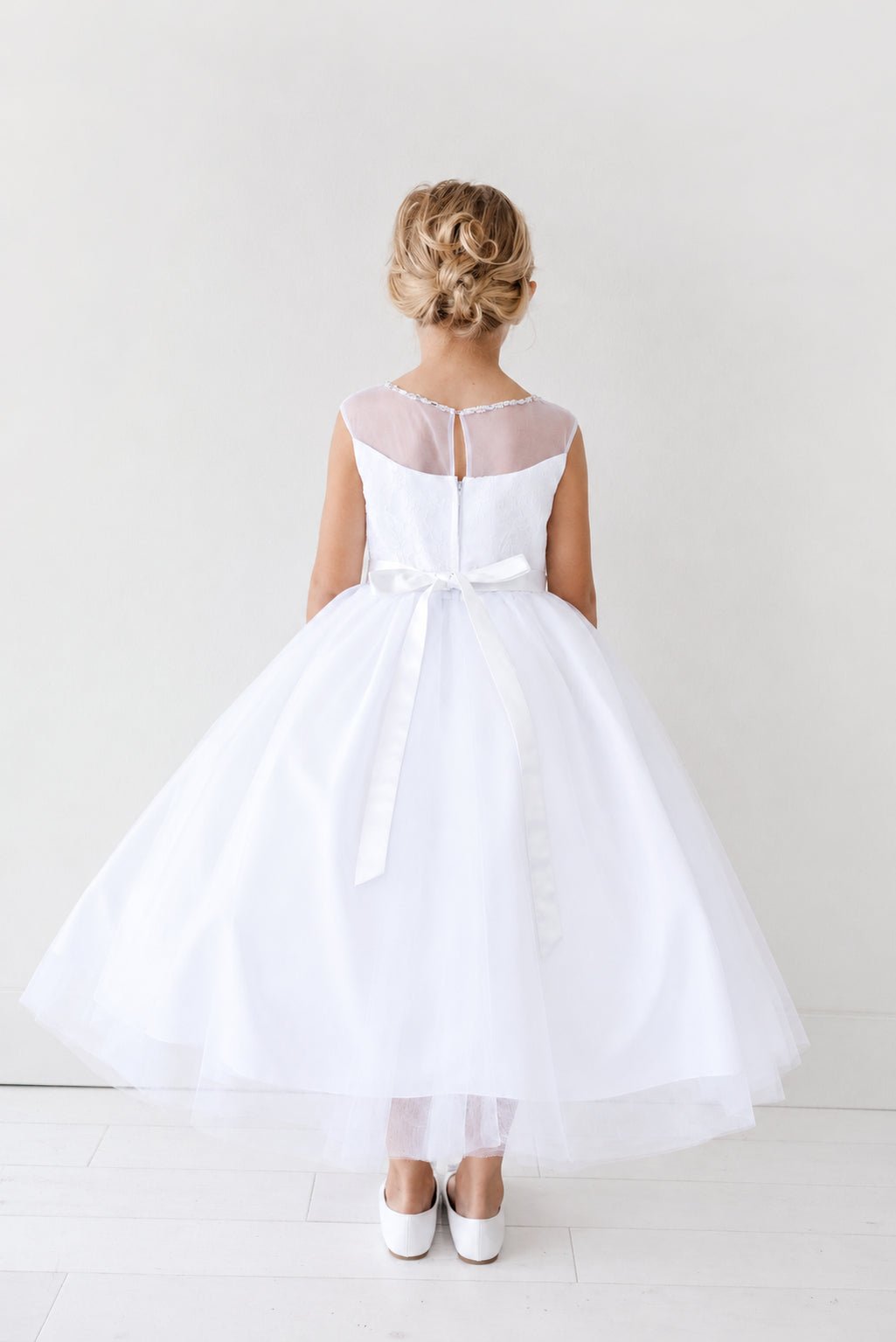 Below the bow, white flower girl dress ribbons trail down the skirt.