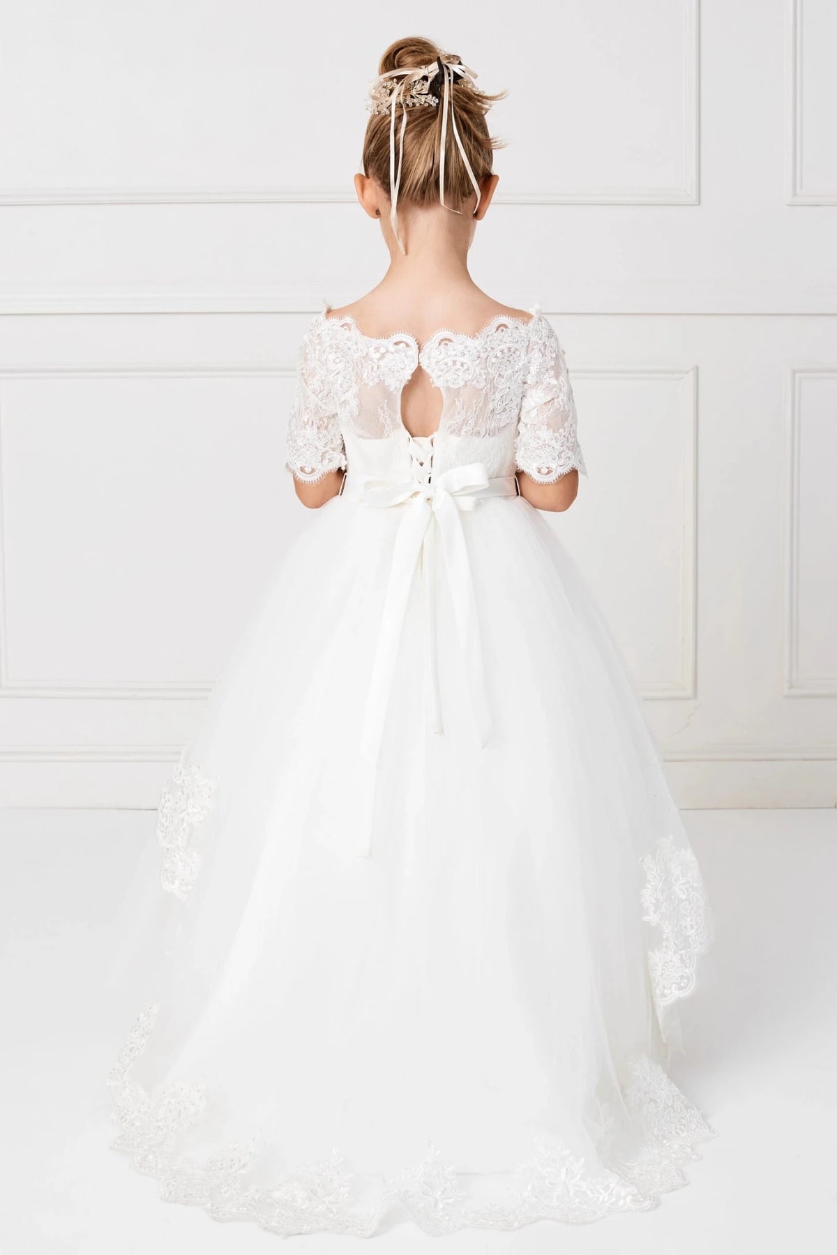 From the waist bow, an off-white flower girl dress sweeps into a lace train.