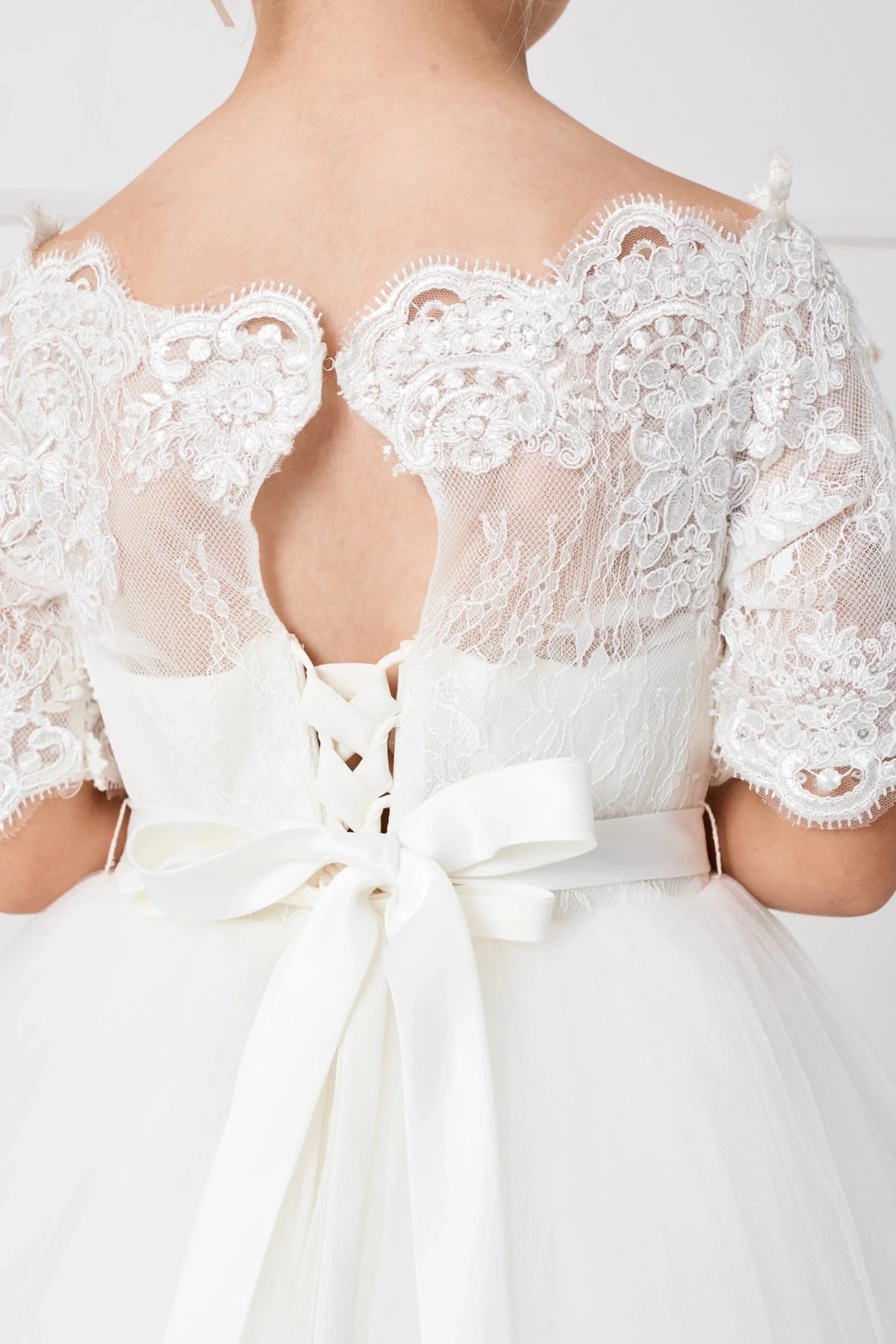 A keyhole interrupts the lace back of this off-white flower girl dress.