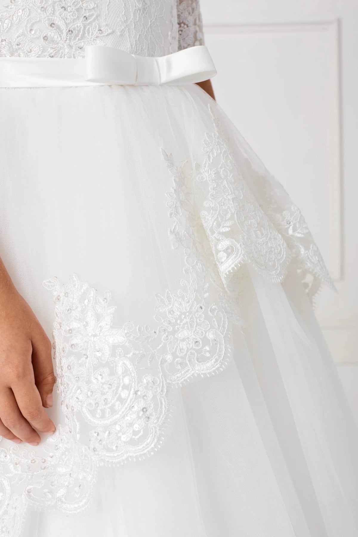 At the hip, off-white flower girl dress lace curves into pointed swags.