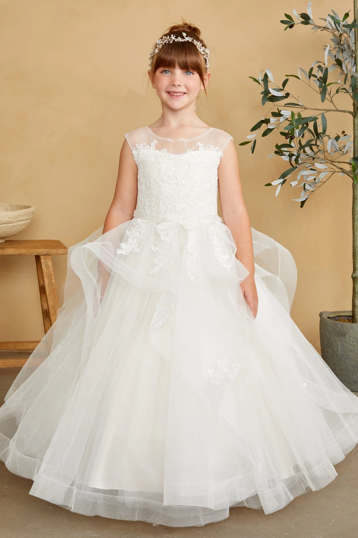Floral appliques follow the off-white flower girl dress's folded overskirt.