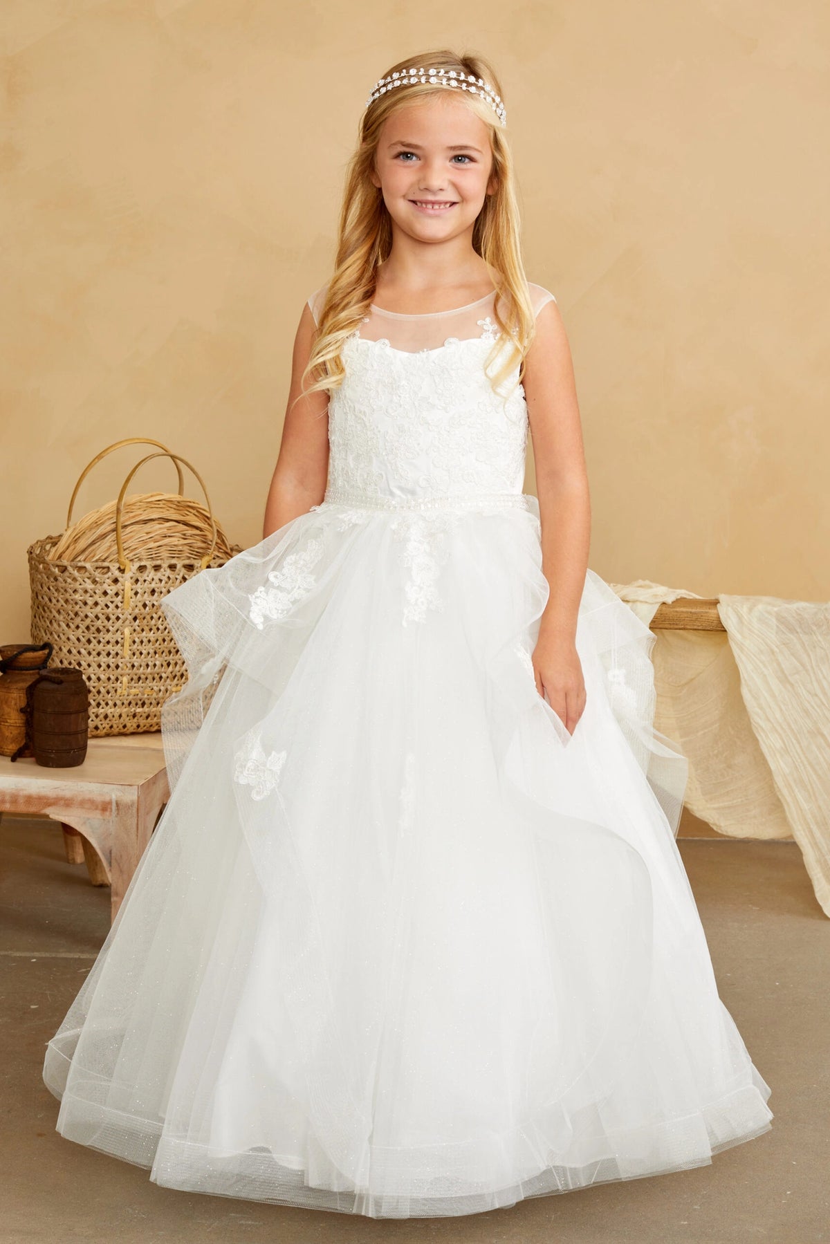 Layered skirt folds spread across the front of an off-white flower girl dress.