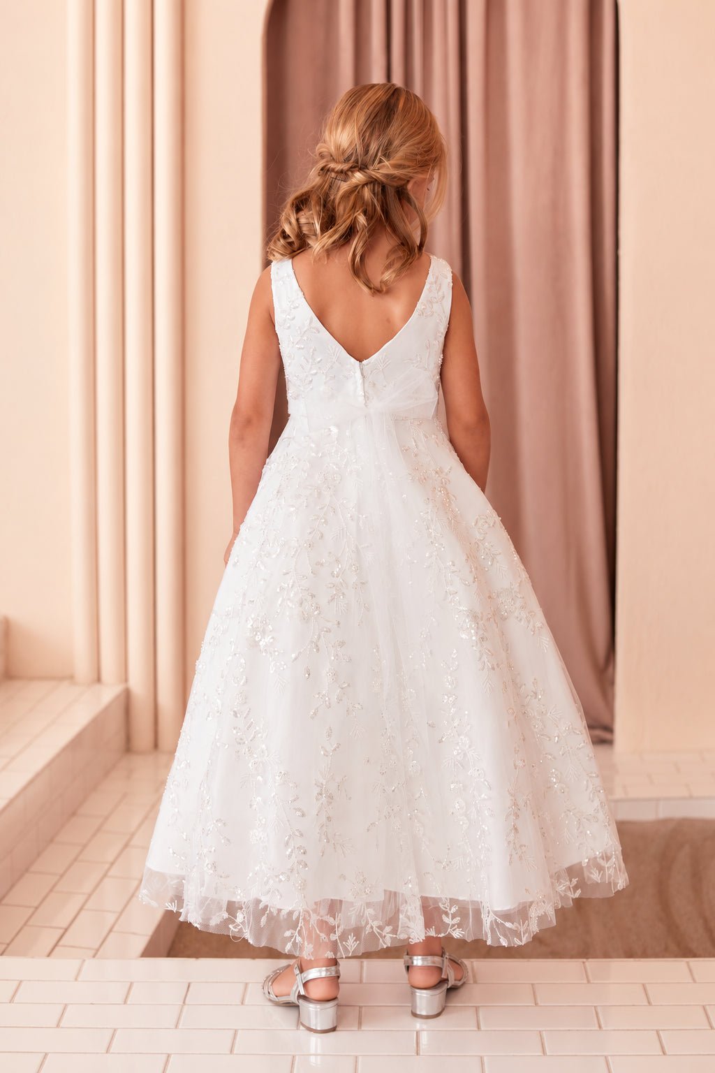 Deep V back above an off-white flower girl dress's embroidered skirt.