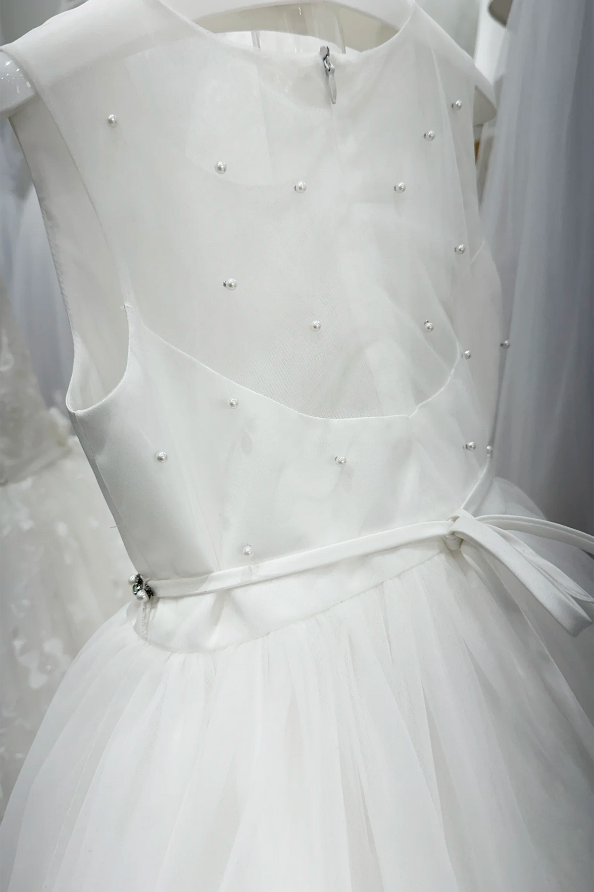 Close-up of the pearl-dotted sheer back, center zipper and narrow satin tie bow on Tiptop 5863 off-white flower girl dress.