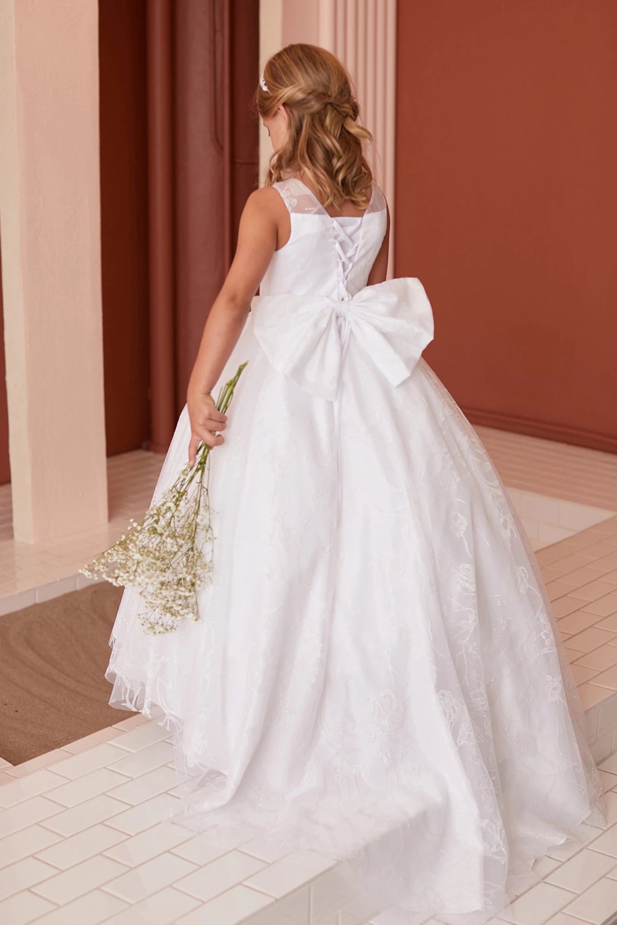 An oversized bow sits above the off-white flower girl dress's lace train.