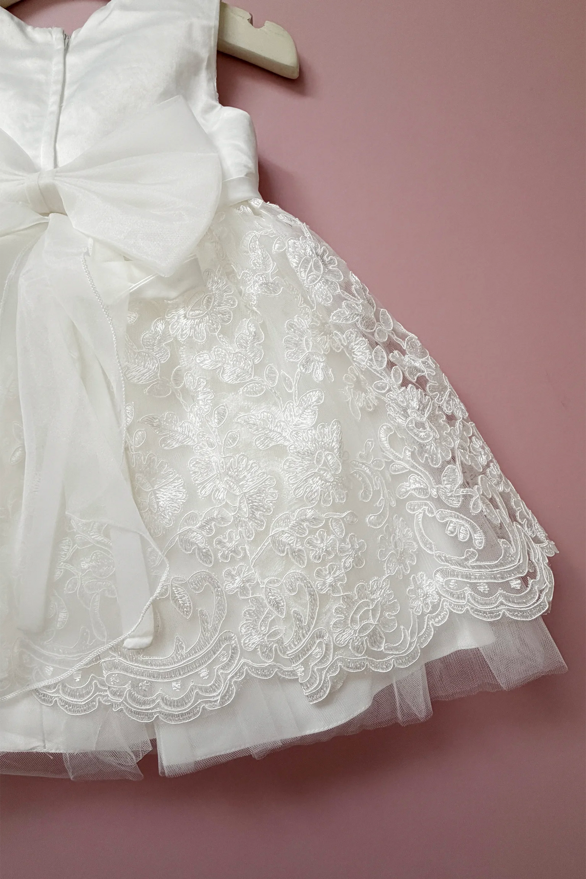 Sheer bow tails drape over the ivory flower girl dress lace skirt.