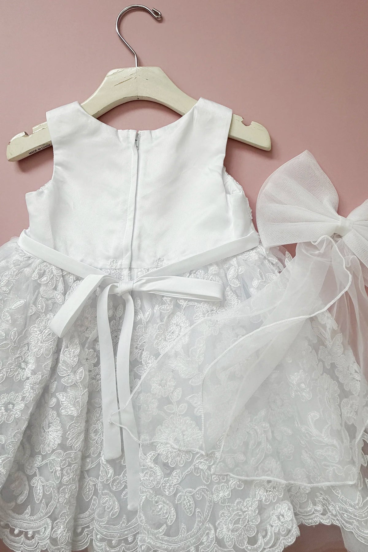 Close-up of the white flower girl dress shows its zipper and tied bow.