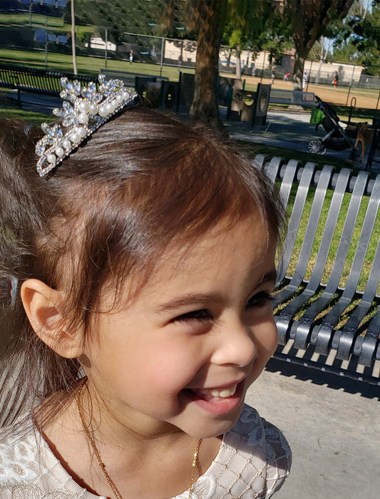 Young girl with a tiara smiling outdoors on a sunny day