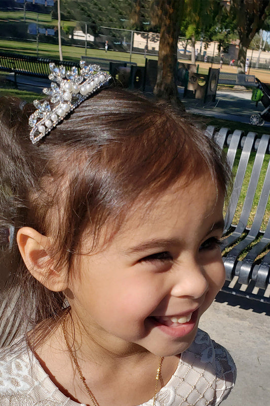 Young girl with a tiara smiling outdoors on a sunny day