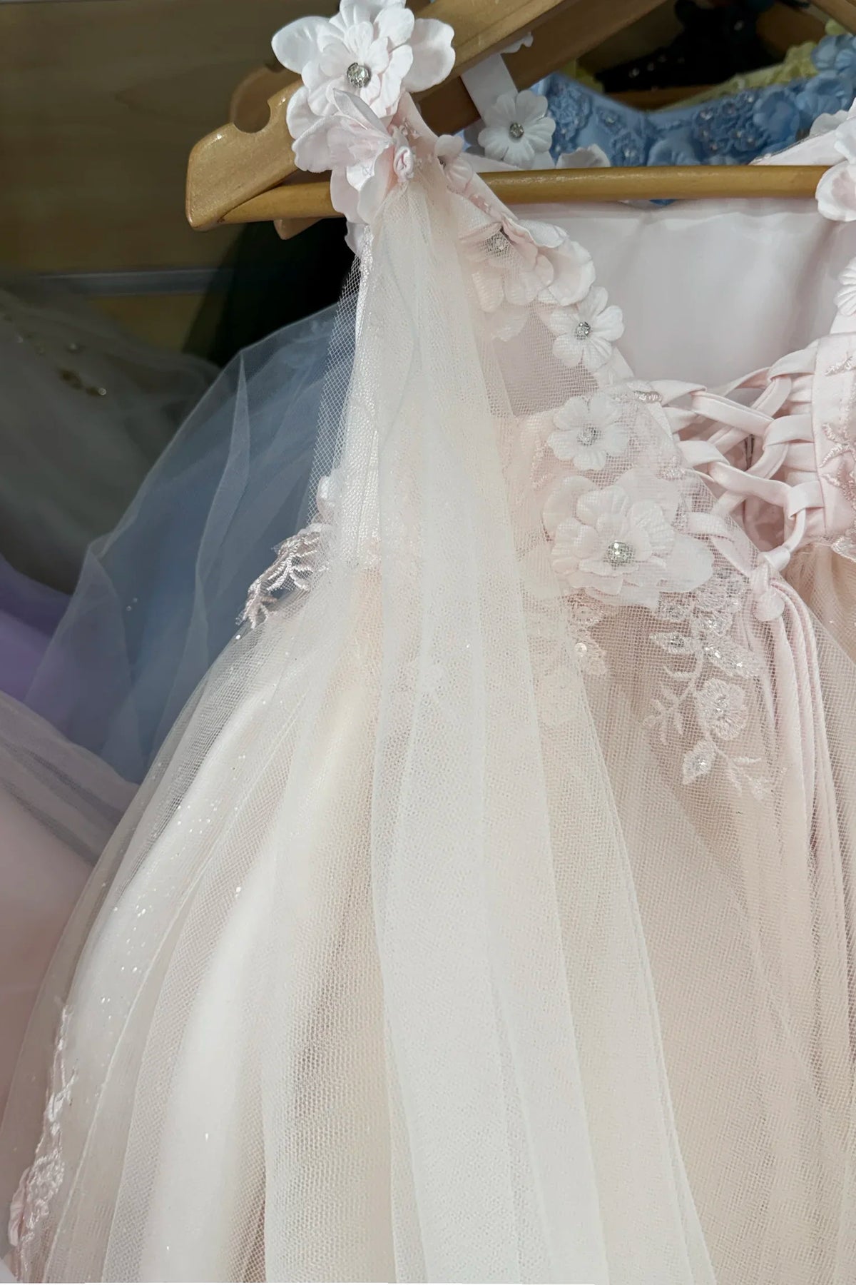 A close-up of a light blush pink tulle dress with floral lace appliques and a matching sheer cape