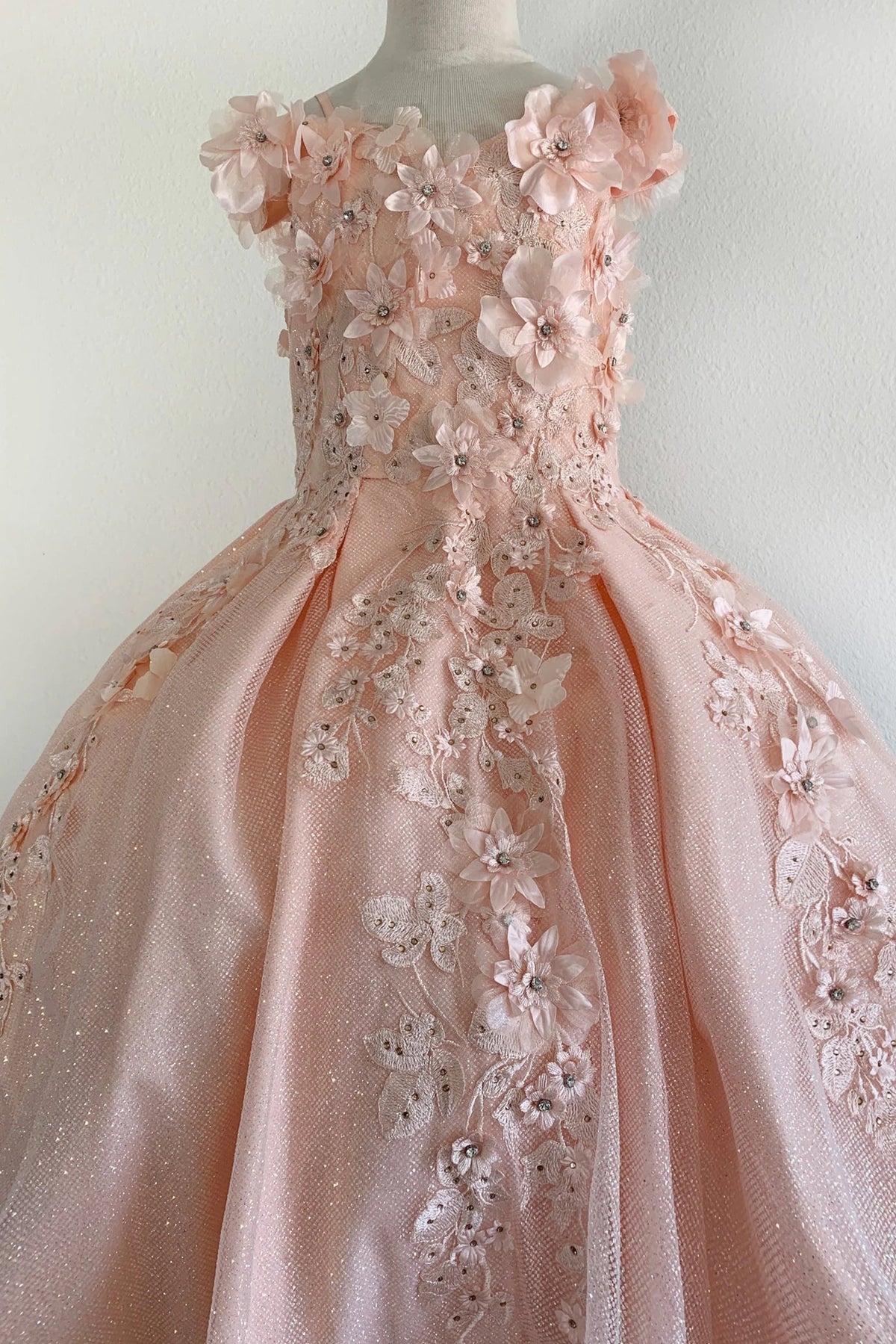 Textured details appear across blush quinceanera ball gown with 3D floral appliques, glitter accents, and voluminous pleated skirt.