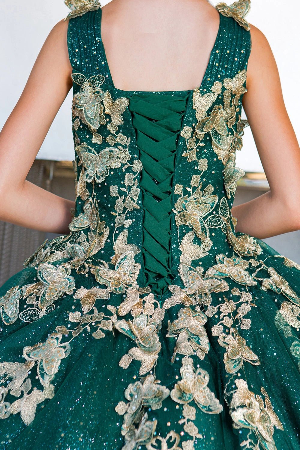 Shown in a back detail, the Hunter Green mini quince dress has lace-up closure framed by gold butterfly and floral appliques.