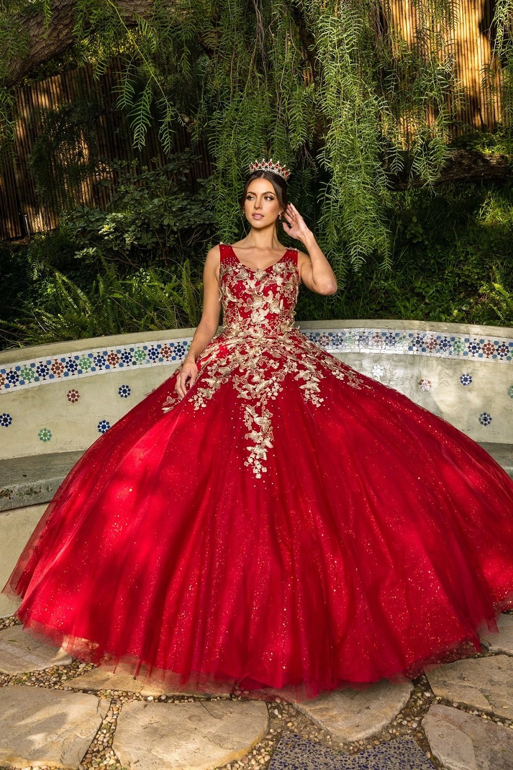 Shown in a front view, the Burgundy quinceañera dress has gold butterfly appliques across the bodice and glitter ball skirt.