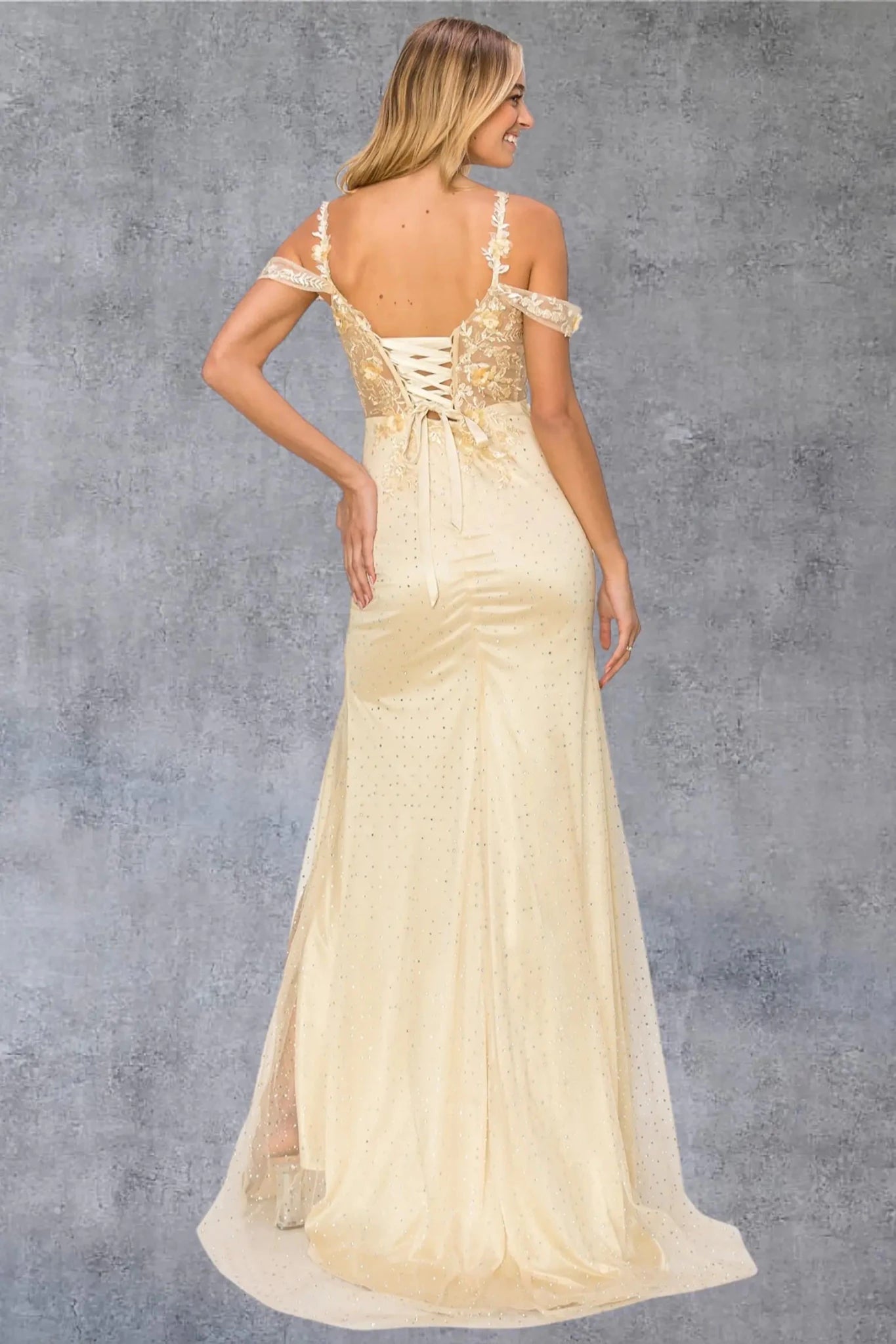 A full-length front view of a woman wearing a champagne formal prom dress featuring a lace-up corset and detachable sleeves.