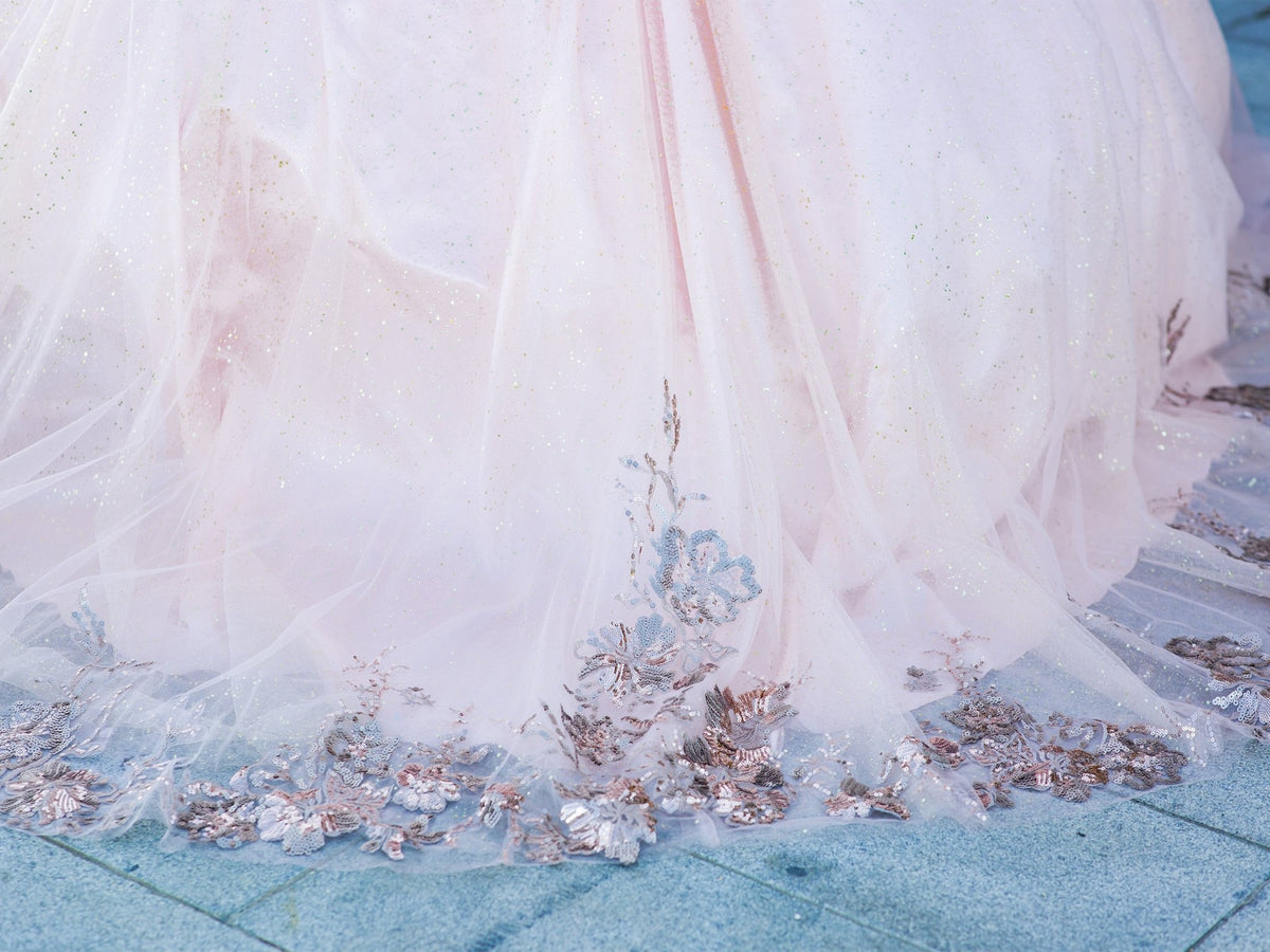 Detailed view highlights blush quinceanera dress tulle with golden lace embroidery and detachable shoulder train sleeve detail.