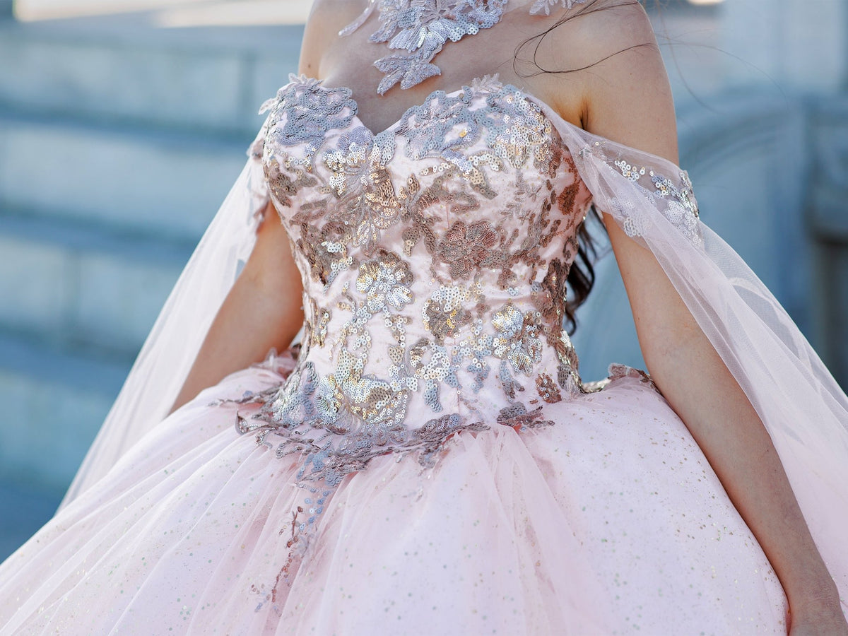 Close-up view reveals blush quinceanera ball gown with golden lace, detachable shoulder train sleeves, and glitter tulle fabric.