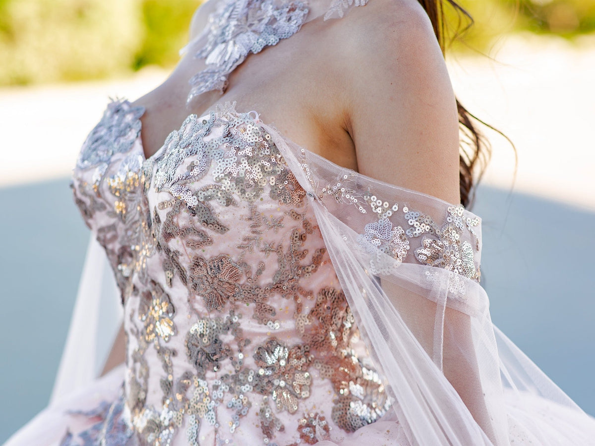 Profile view highlights detail of a blush quinceanera ball gown with golden lace, detachable shoulder train sleeves.