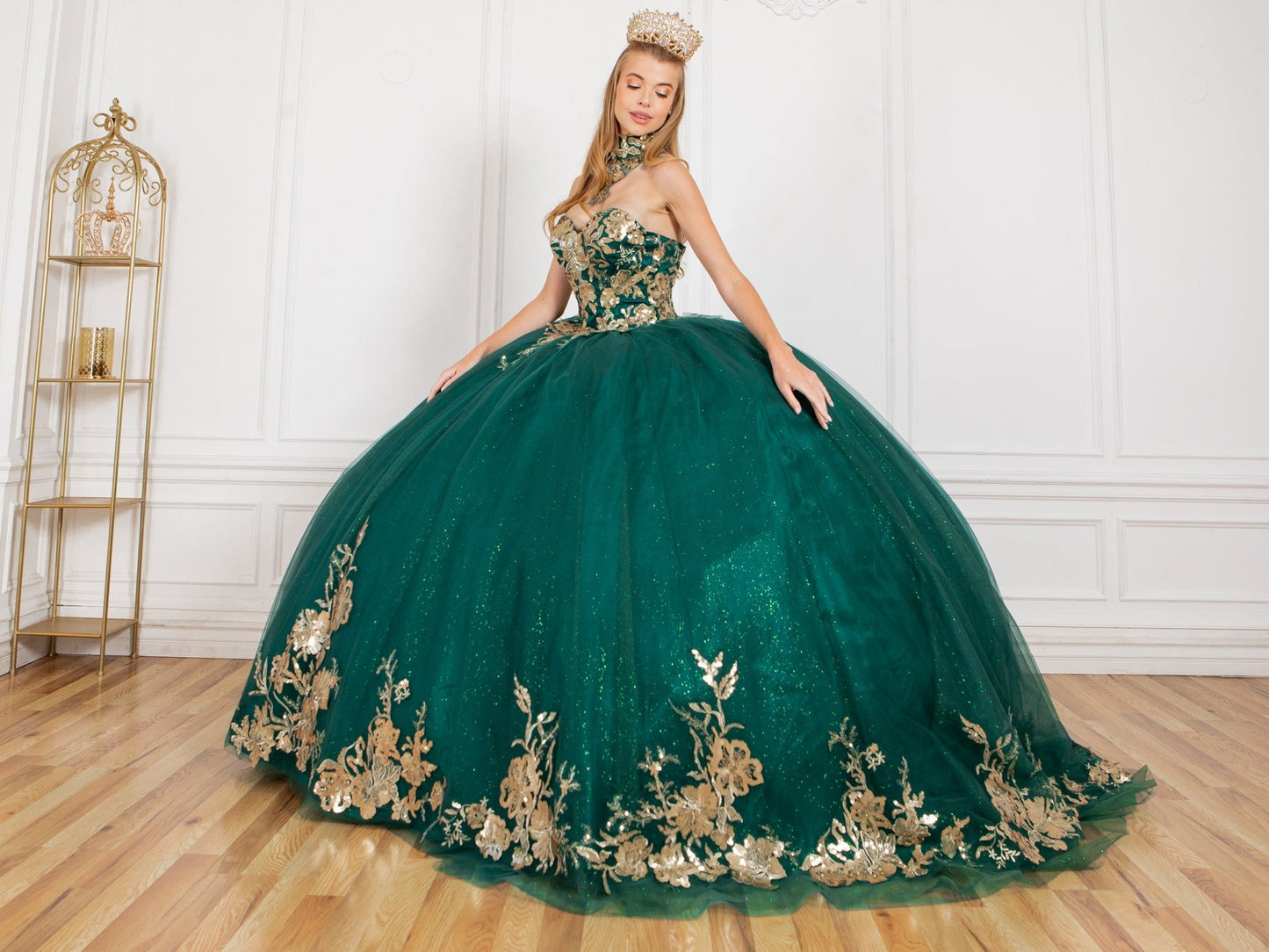 Front side view of a woman wearing hunter green quinceanera ball gown with golden lace, detachable shoulder train sleeves, and tiara accent