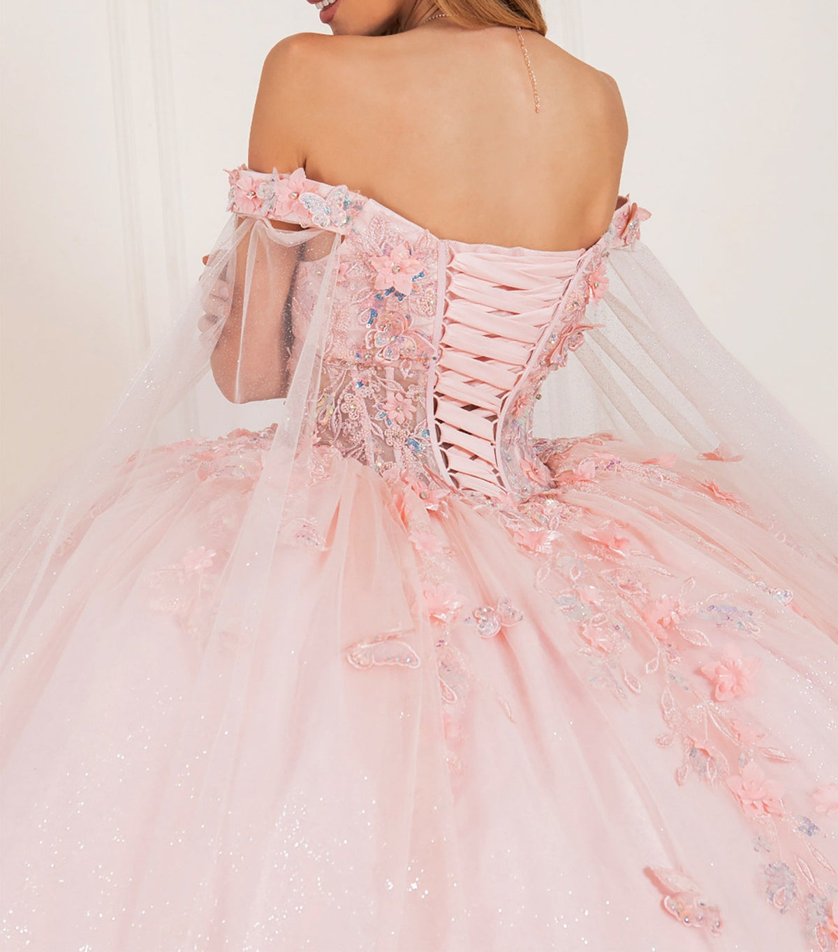 Back view of a woman wearing blush quinceanera dress with floral lace appliques, off-shoulder neckline, and tulle skirt